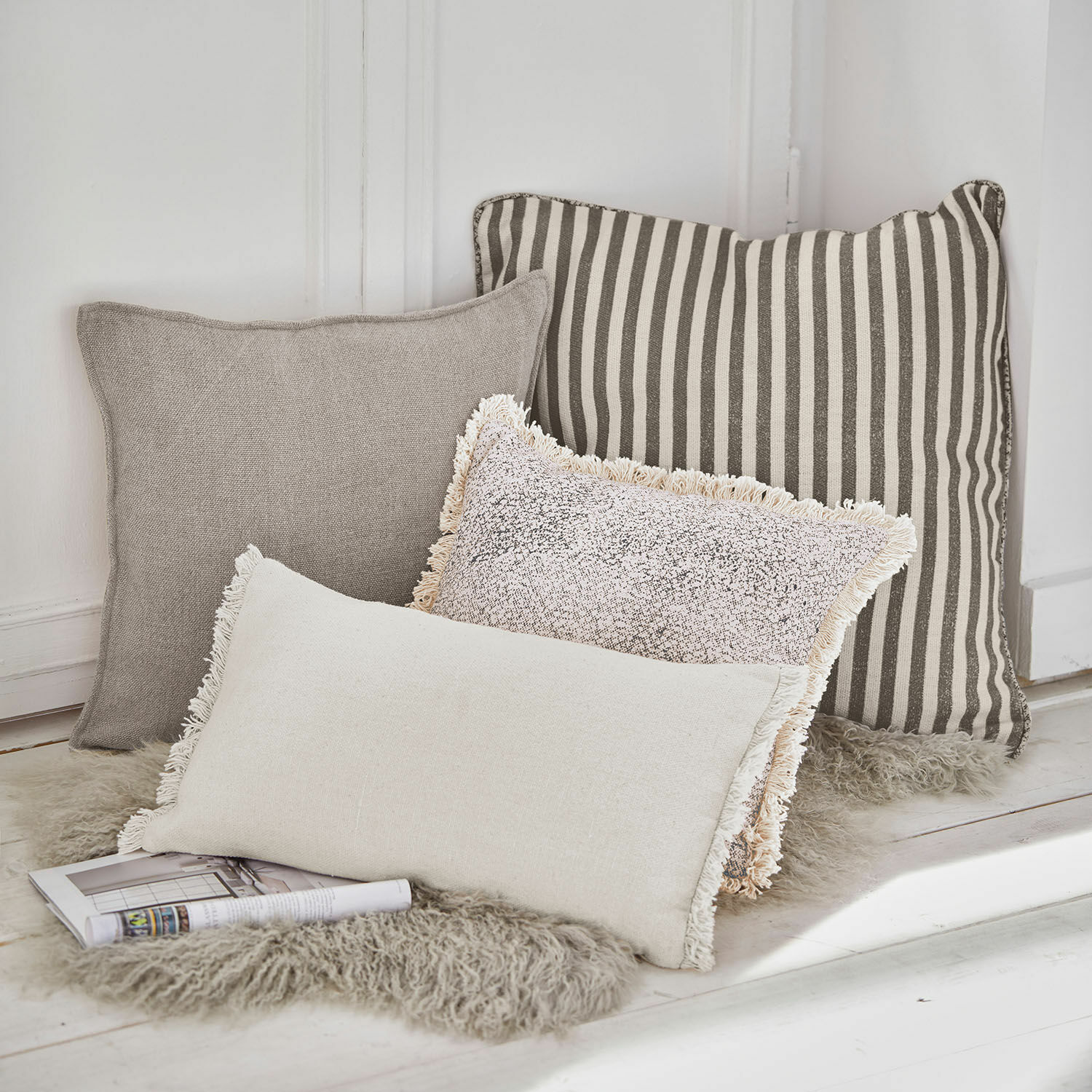 Kissen 4er Set Valenciennes Vier dekorative Kissen in Beige- und Grautönen auf flauschigem Fellteppich arrangiert