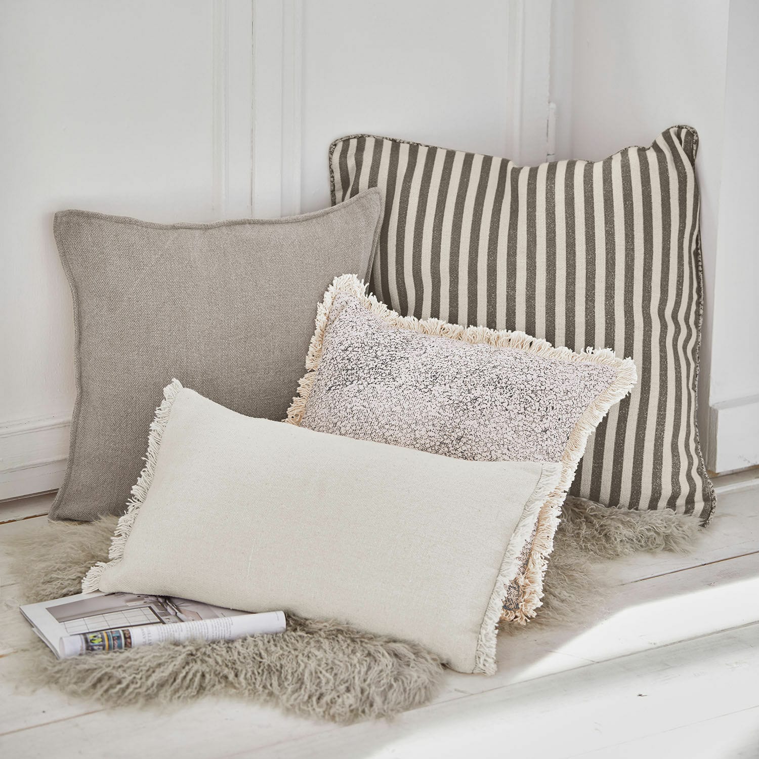 Kissen 4er Set Valenciennes Vier dekorative Kissen in Beige- und Grautönen auf flauschigem Fellteppich arrangiert