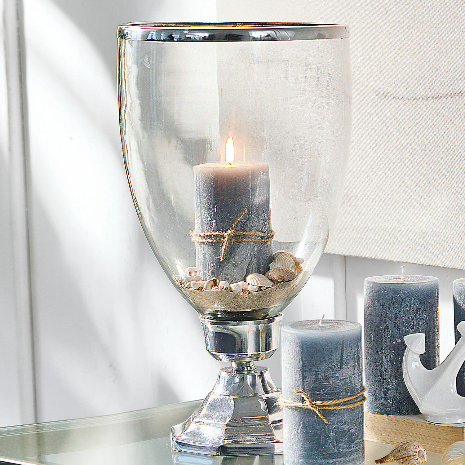 Kerzenständer Echelon Graue Kerze mit Juteschnur in Glaswindlicht mit Muscheln und Sand auf dem Tisch