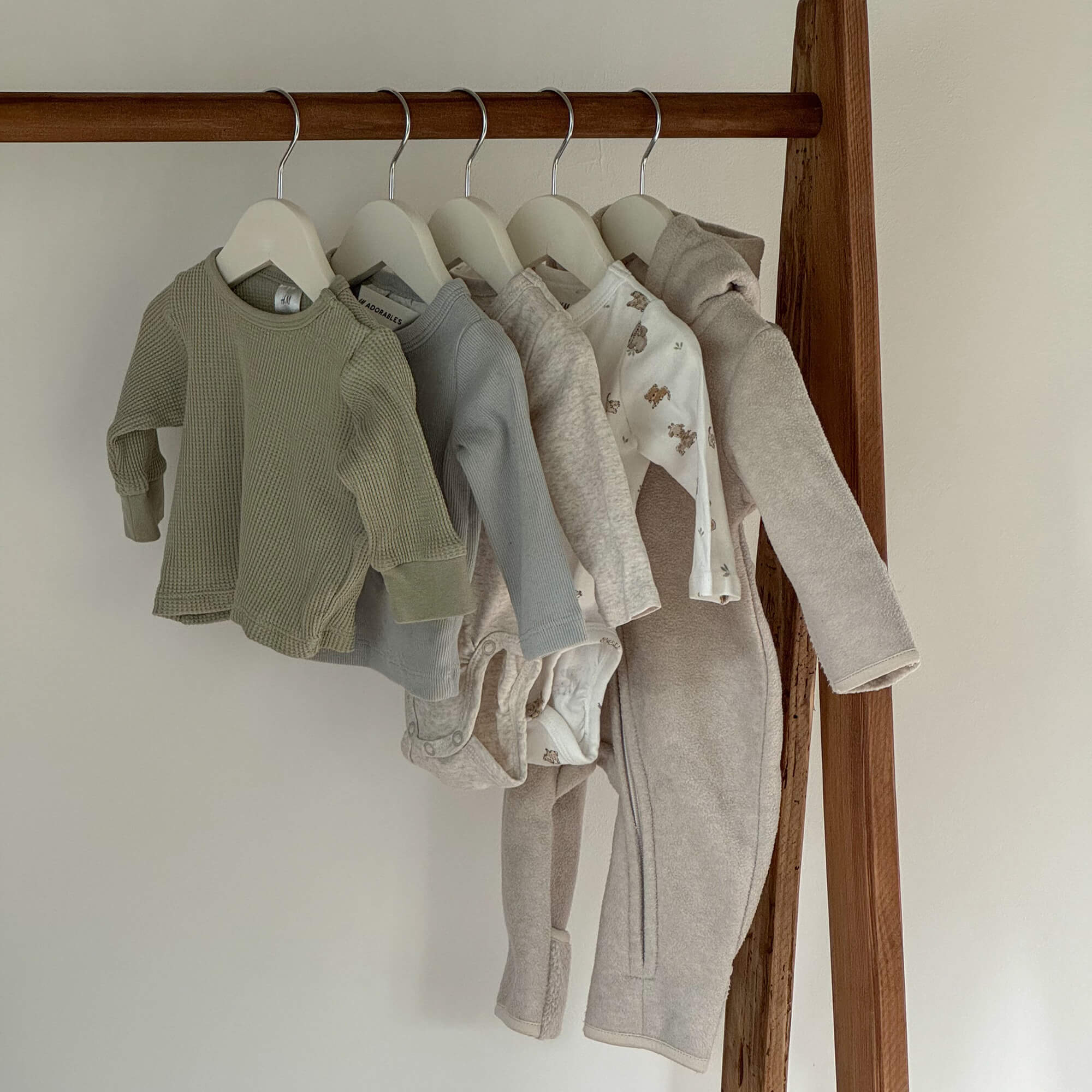 Set aus Babybekleidung in neutralen Farben an Kleiderbügeln, weiche Stoffe mit Bärenmotiven