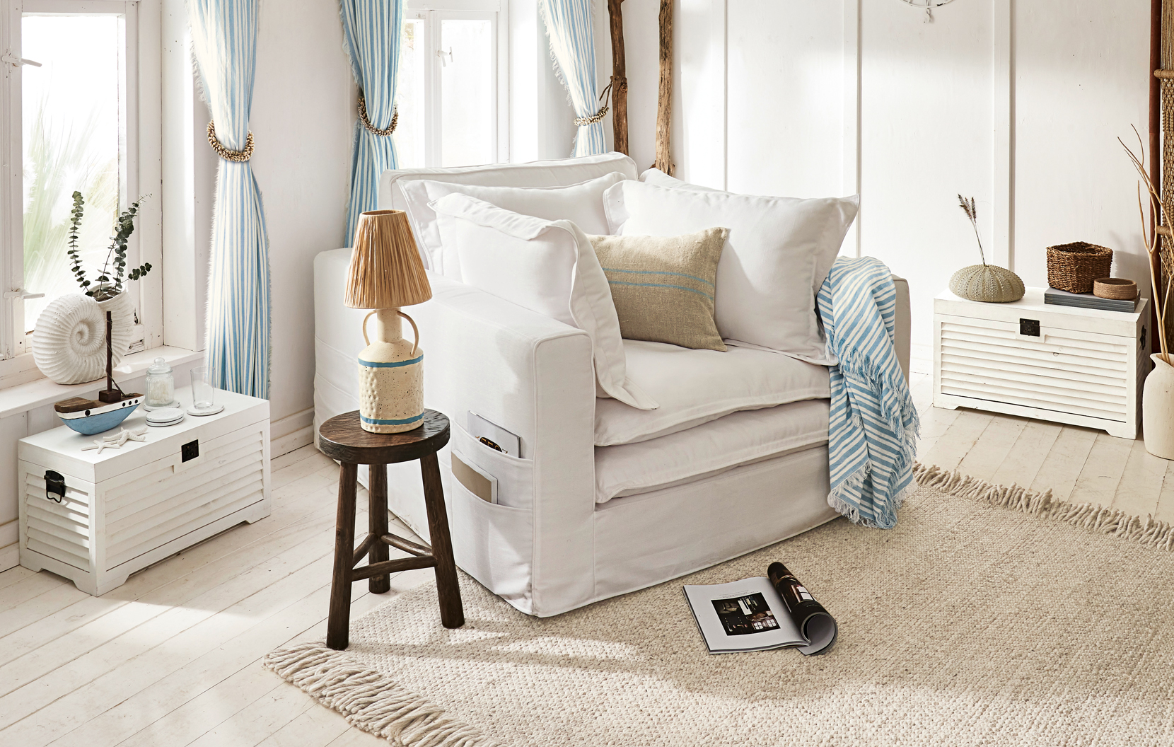 Gemütlicher weisser Sessel mit Kissen und blau-weiss gestreiftem Plaid in hellem, maritimem Wohnzimmer