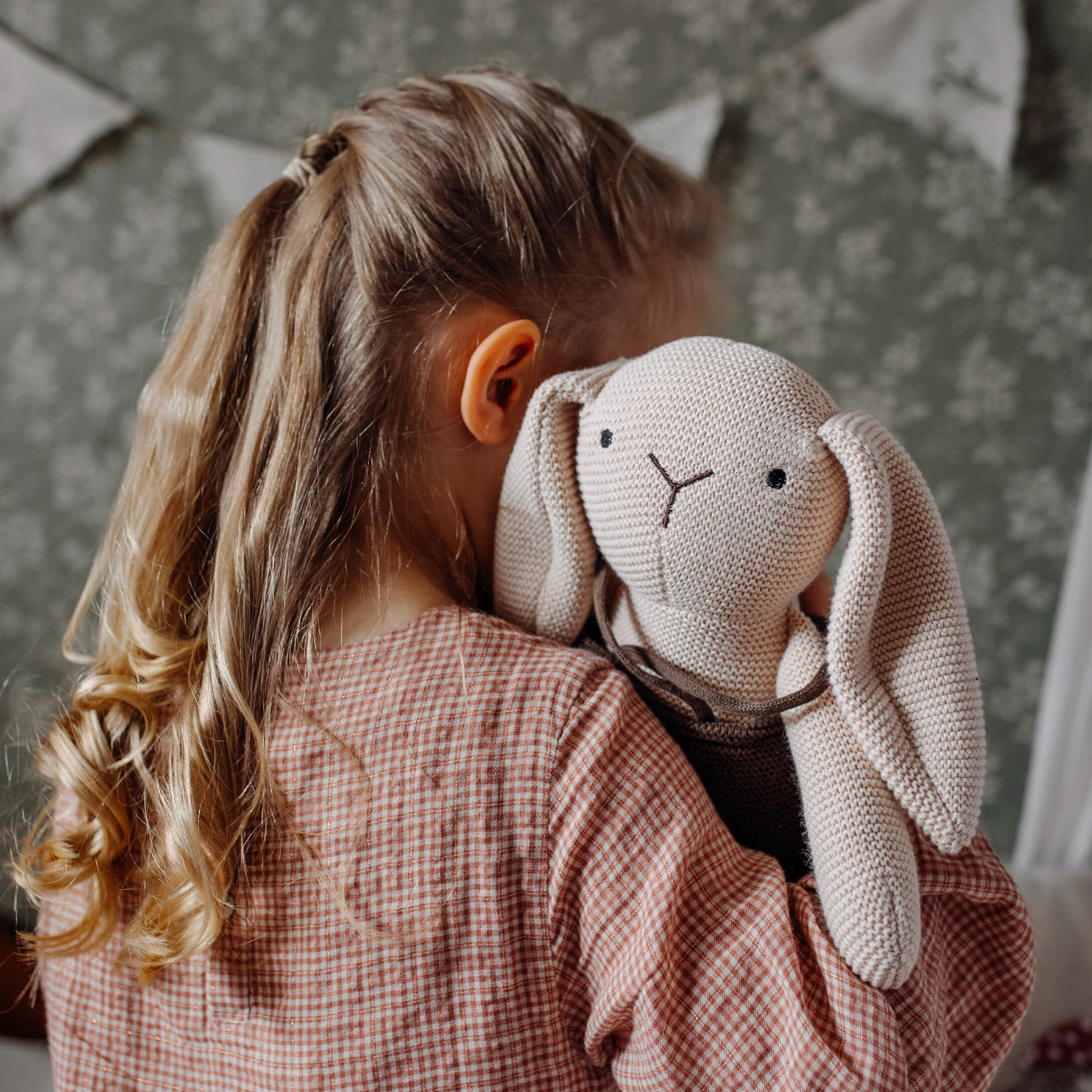 Mädchen umarmt beigefarbenen gestrickten Kuschelhasen im Kinderzimmer