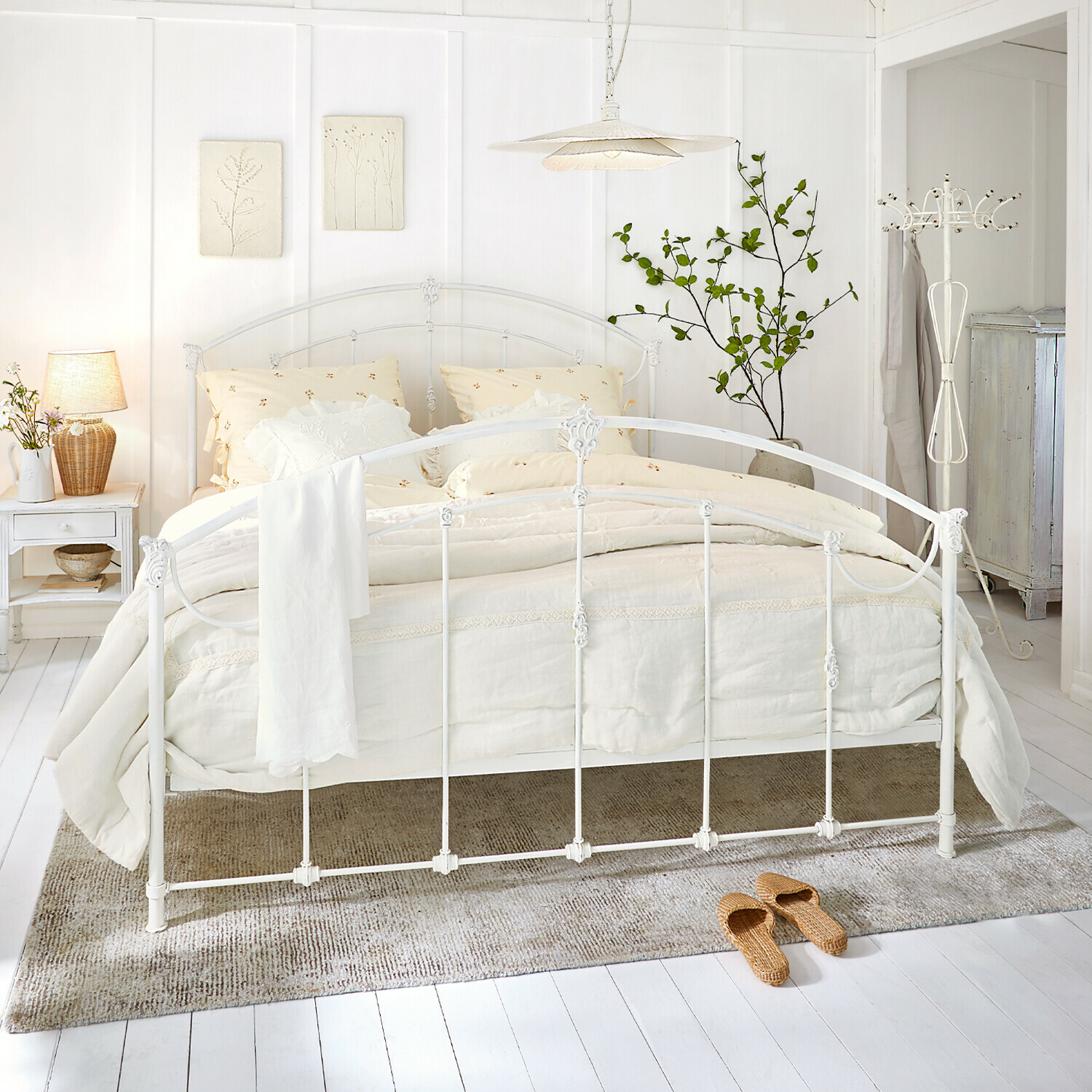 Bett Canefield Weisses Metallbett mit cremefarbiger Bettwäsche und Naturteppich in hellem Schlafzimmer