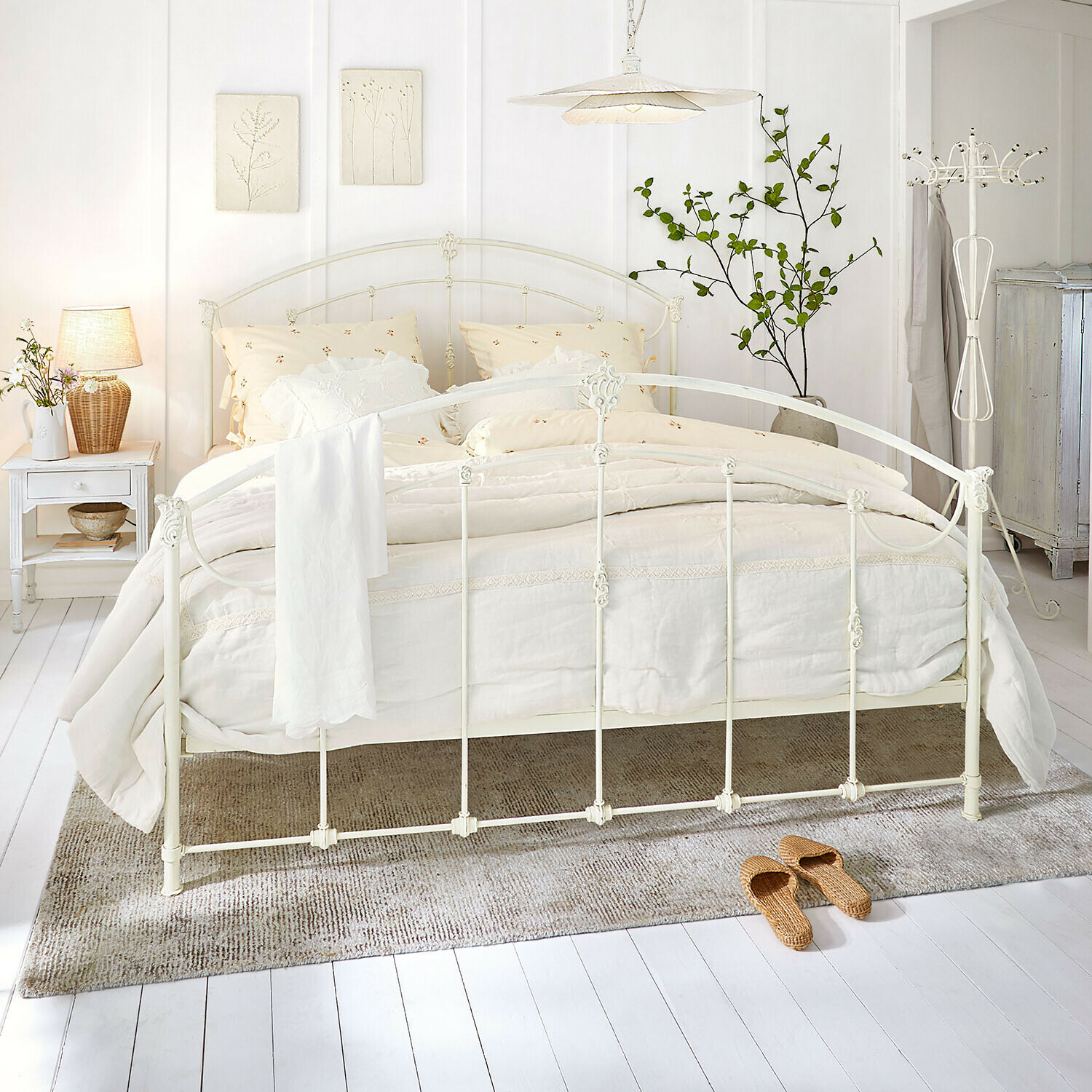 Bett Canefield Weisses Metallbett mit cremefarbiger Bettwäsche und Naturteppich in hellem Schlafzimmer