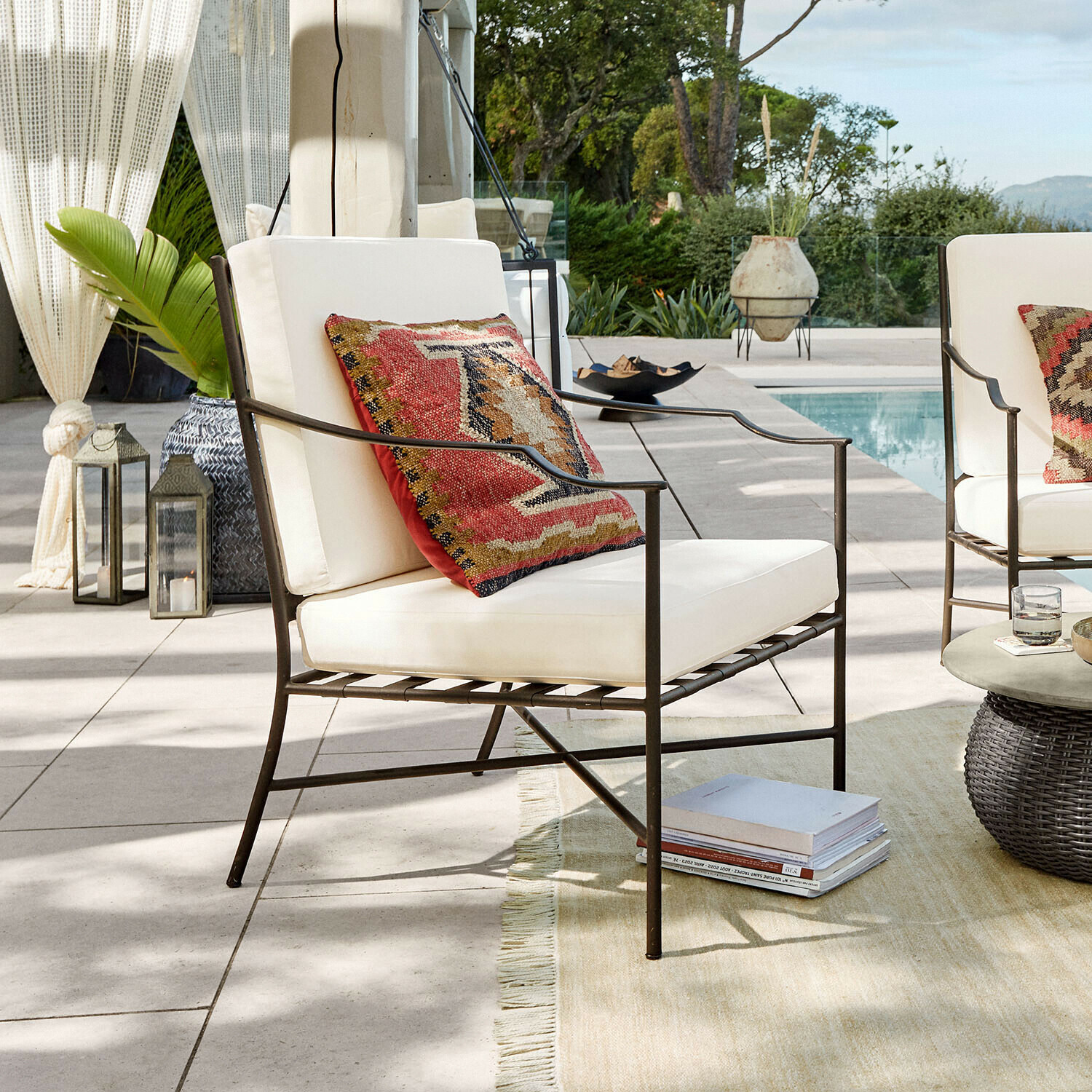 Sessel Vexford Metall-Gartenstuhl mit cremefarbenen Polstern und buntem Dekokissen am Pool