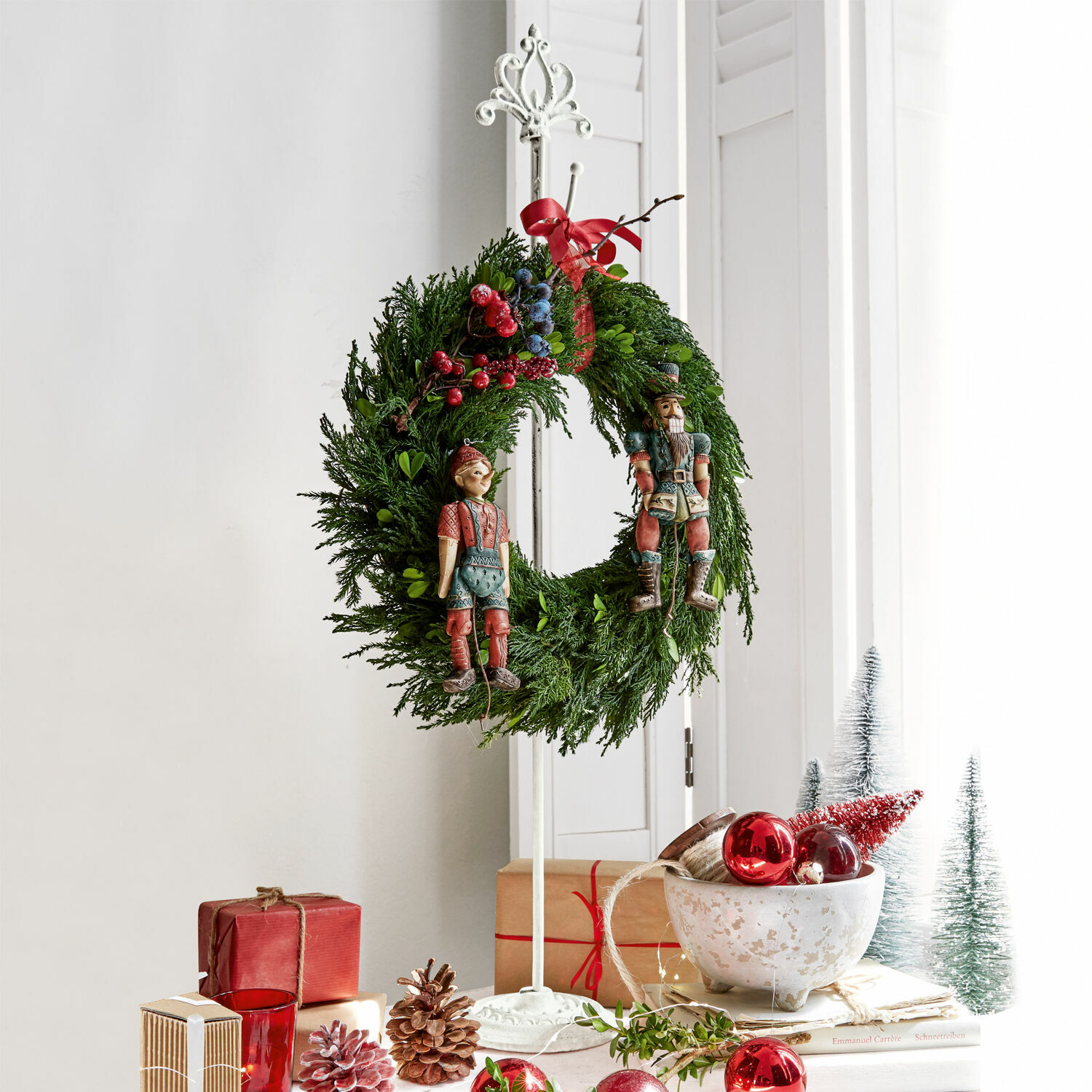 Kranzständer Irulan Weihnachtskranz aus grünen Zweigen mit roten und blauen Beeren sowie Holzfiguren auf weissem Ständer