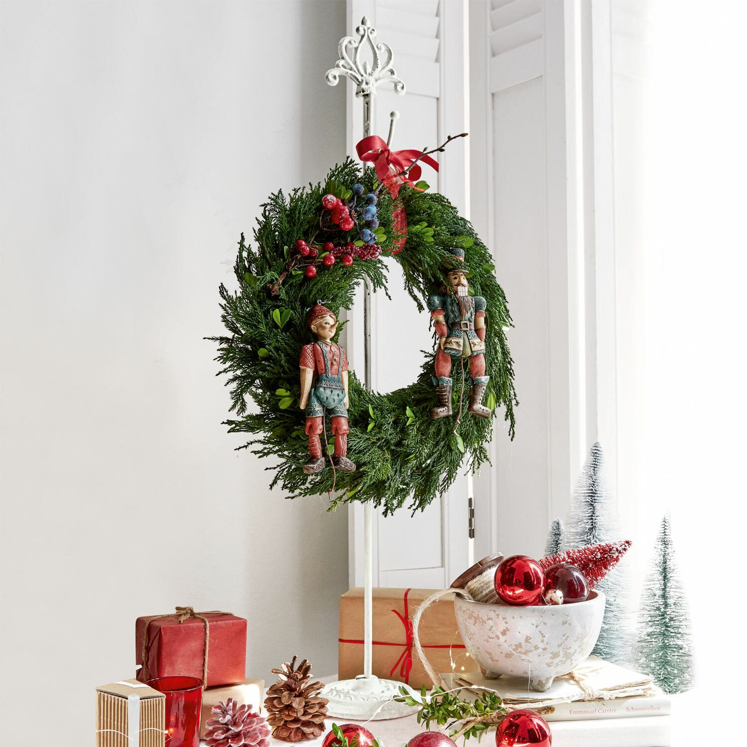 Kranzständer Irulan Weihnachtskranz aus grünen Zweigen mit roten und blauen Beeren sowie Holzfiguren auf weissem Ständer