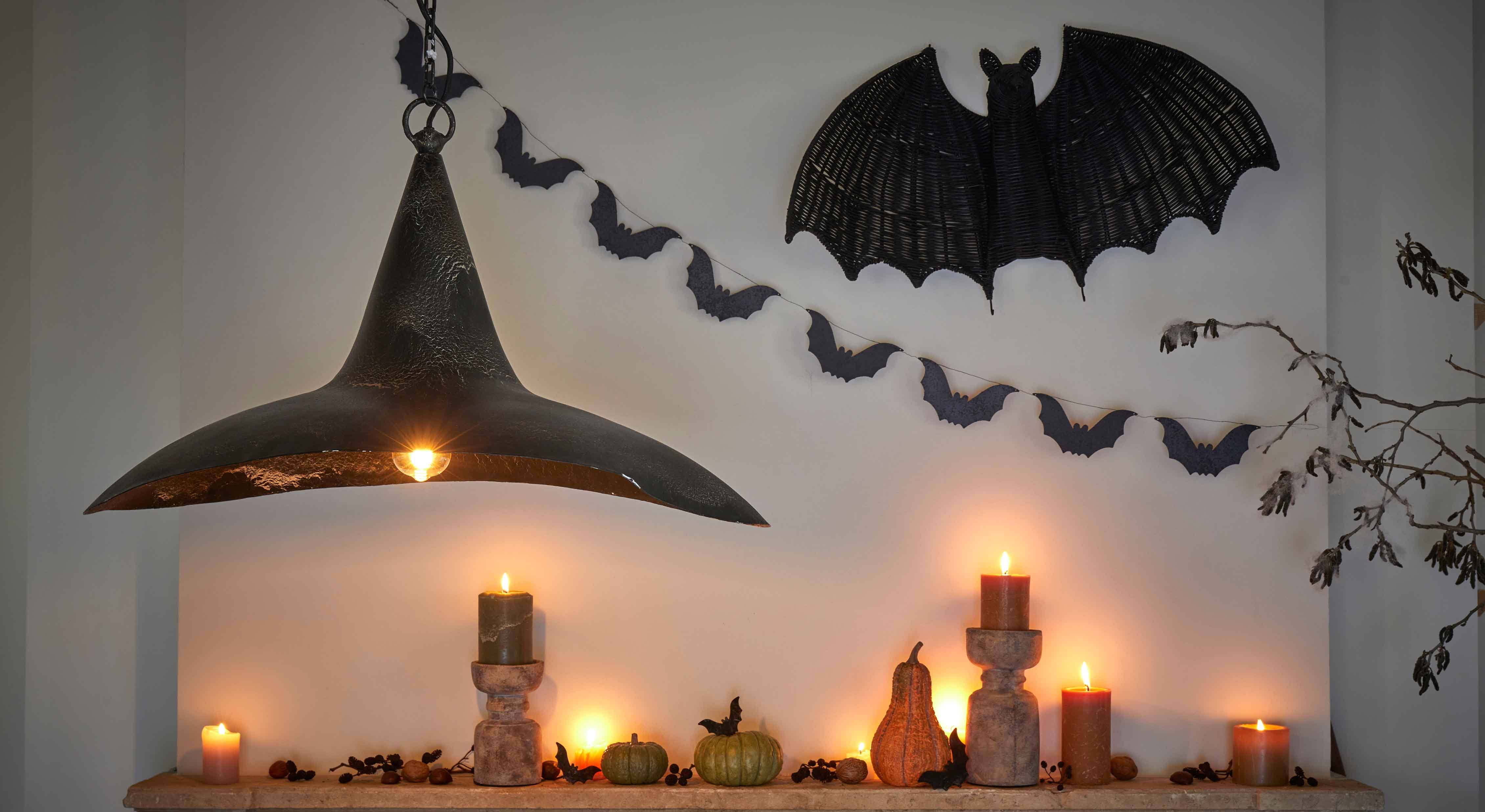 Halloween-Dekoration mit schwarzen Kerzen, Kürbissen und schwarzer Metalllampe an Wand mit Fledermäusen