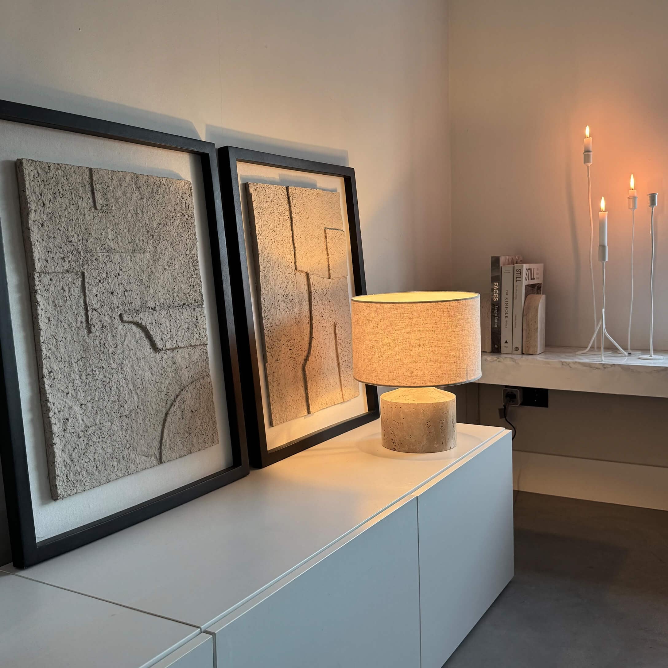 Moderne Tischlampe mit beigem Schirm und Steinsockel auf weissem Sideboard mit Wanddekoration