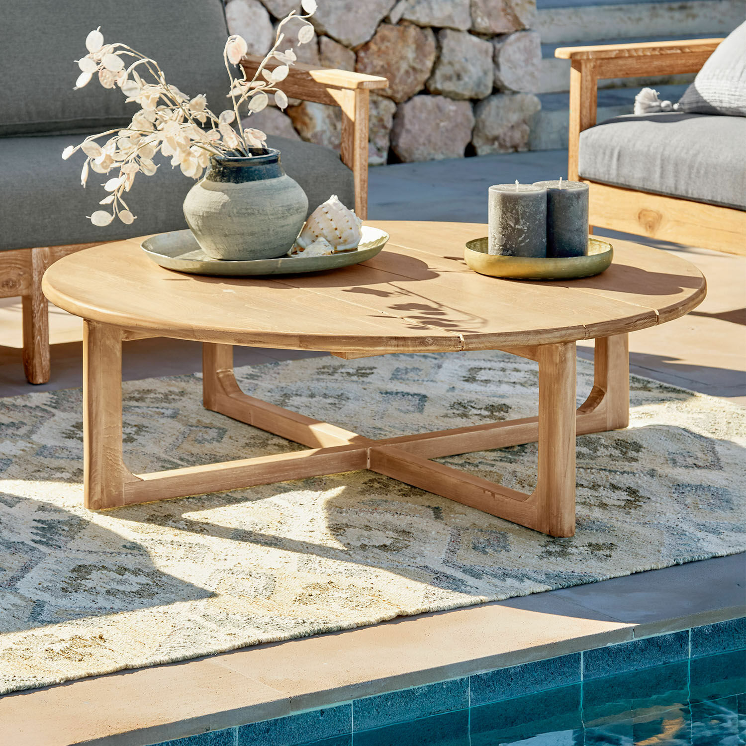 Couchtisch Tewksbury Runder Couchtisch aus naturbelassenem Teakholz auf der Terrasse am Pool mit Dekorationen