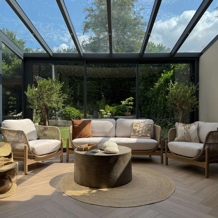 Gemütliches Wohnzimmer mit hellen Holz- und Stoffsofas unter Glasdach, runder Naturfaserteppich