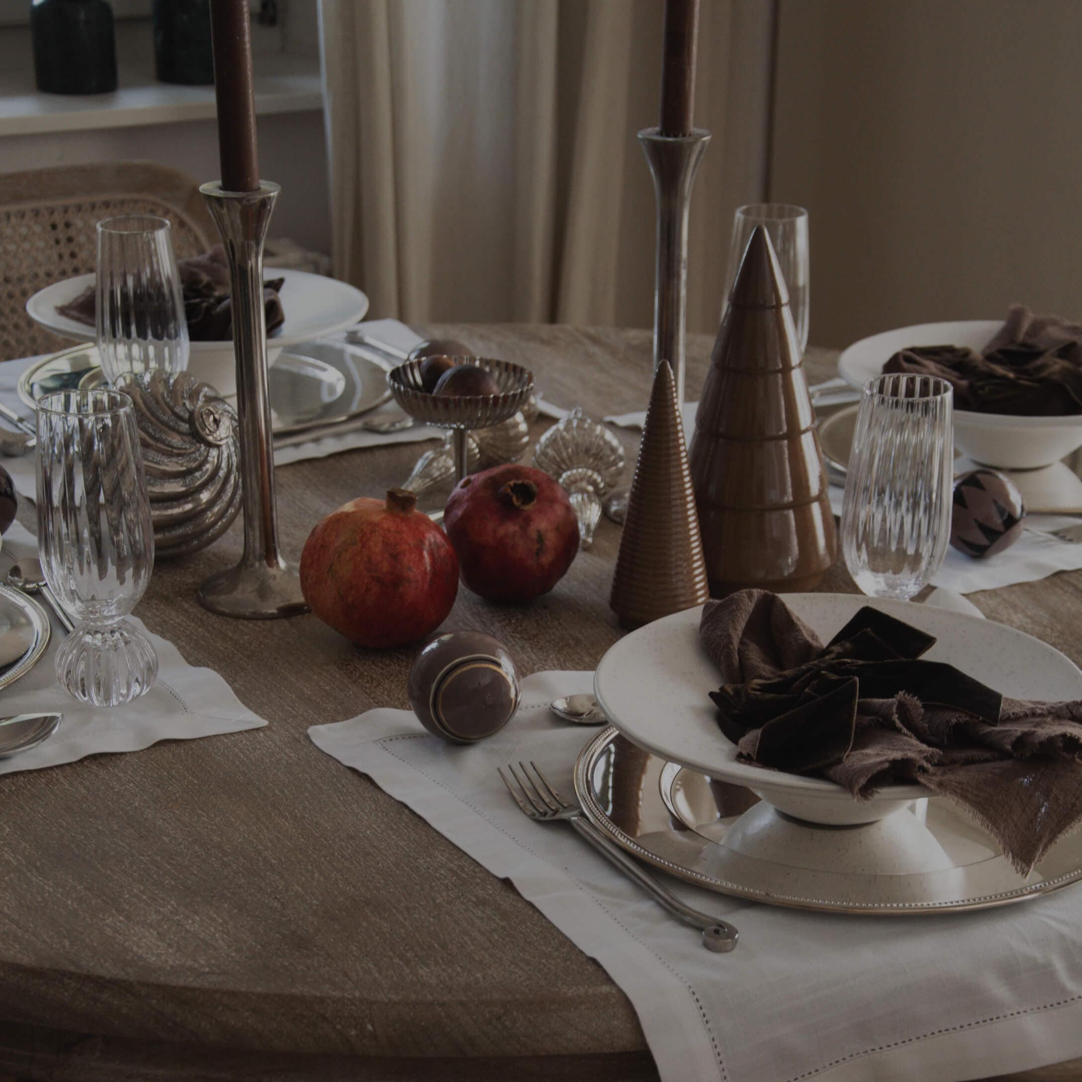 Eleganter Esstisch mit braunen Keramikkegeln, braunen Stoffservietten und roten Granatäpfeln