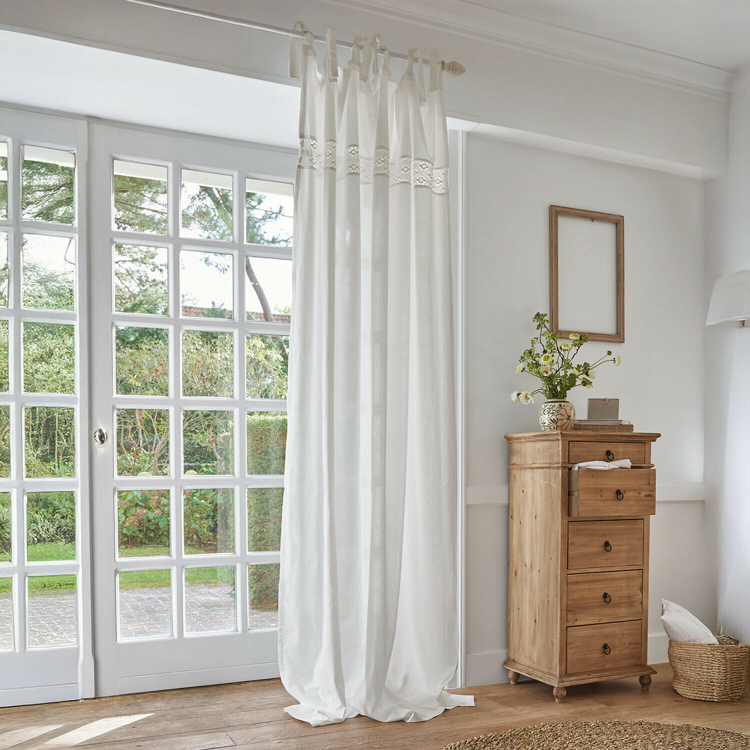 Weisse Baumwollgardine mit Spitzenband in hellem Raum mit natürlicher Holzkommode