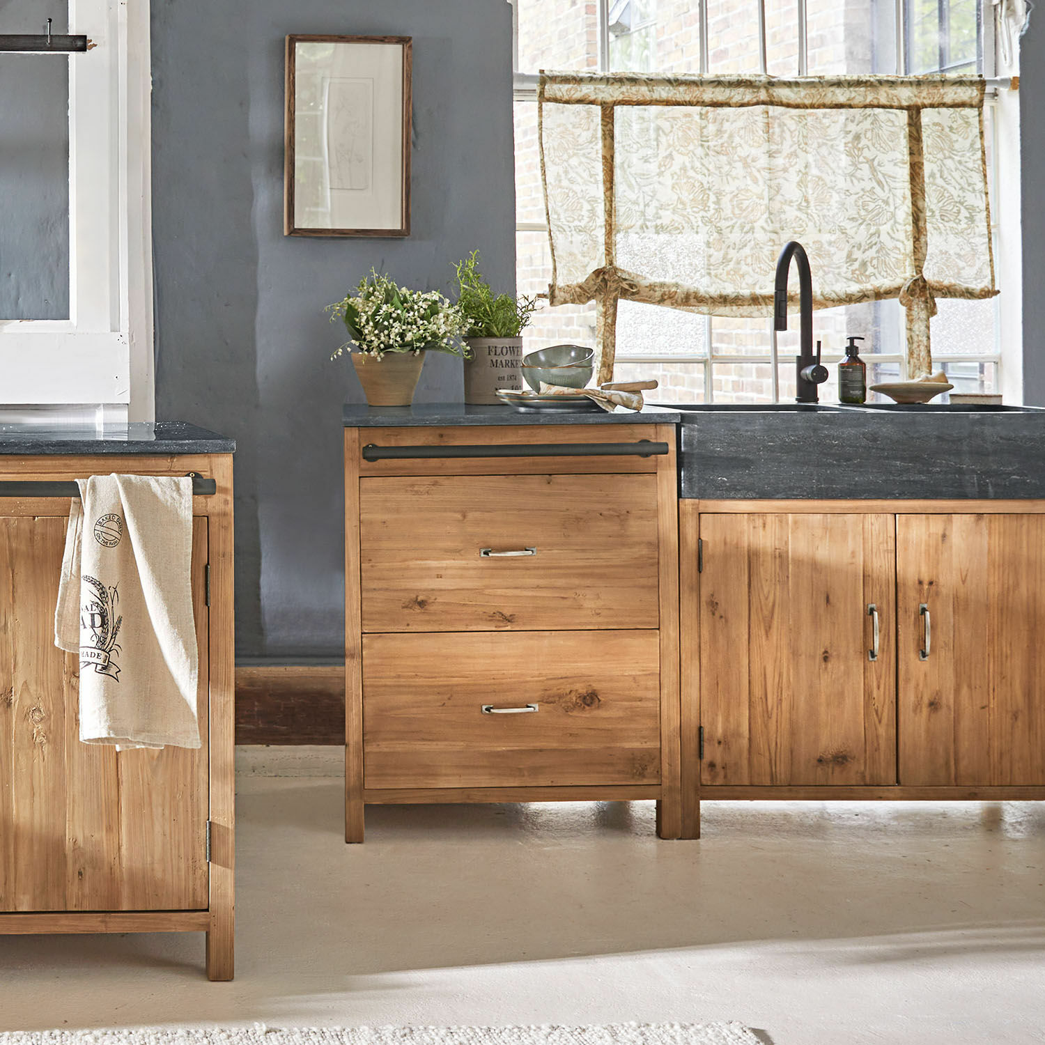 Unterschrank Sunnybrook Küche mit Holzschränken und schwarzer Arbeitsplatte, Pflanzen und floralen Vorhängen als Dekoration