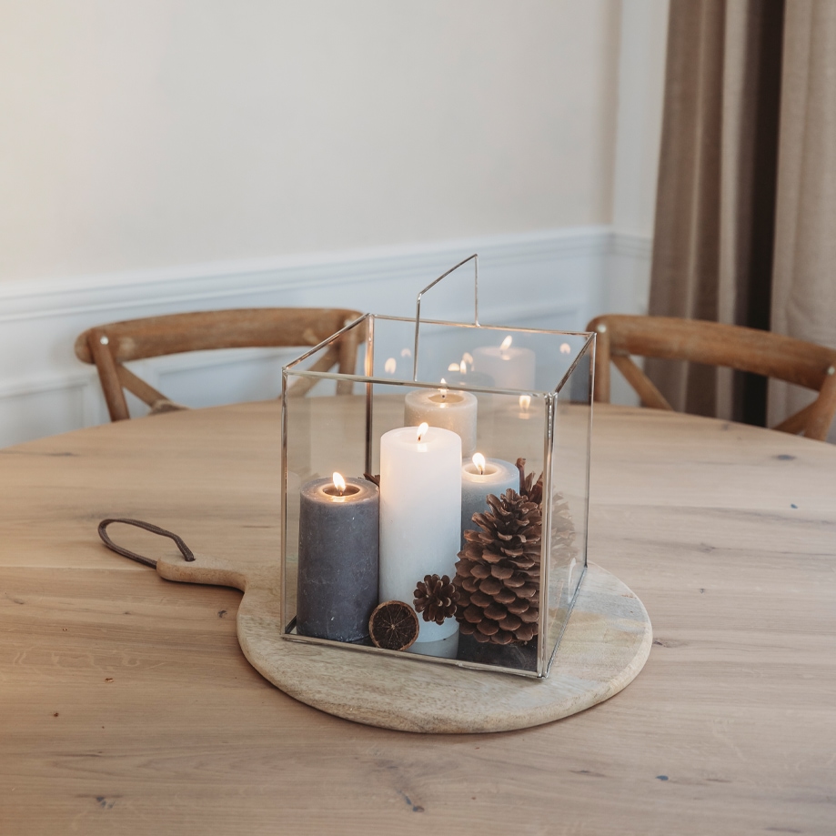 Glaslaterne mit drei Kerzen und Kiefernzapfen auf Holzbrett als Weihnachtsdekoration auf dem Tisch