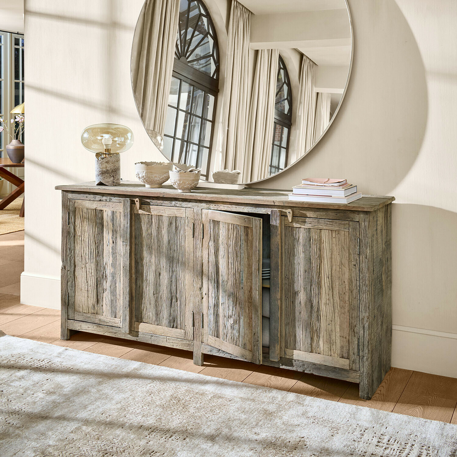 Rustikaler grauer Holz-Sideboard mit vier Türen und rundem dekorativem Wandspiegel