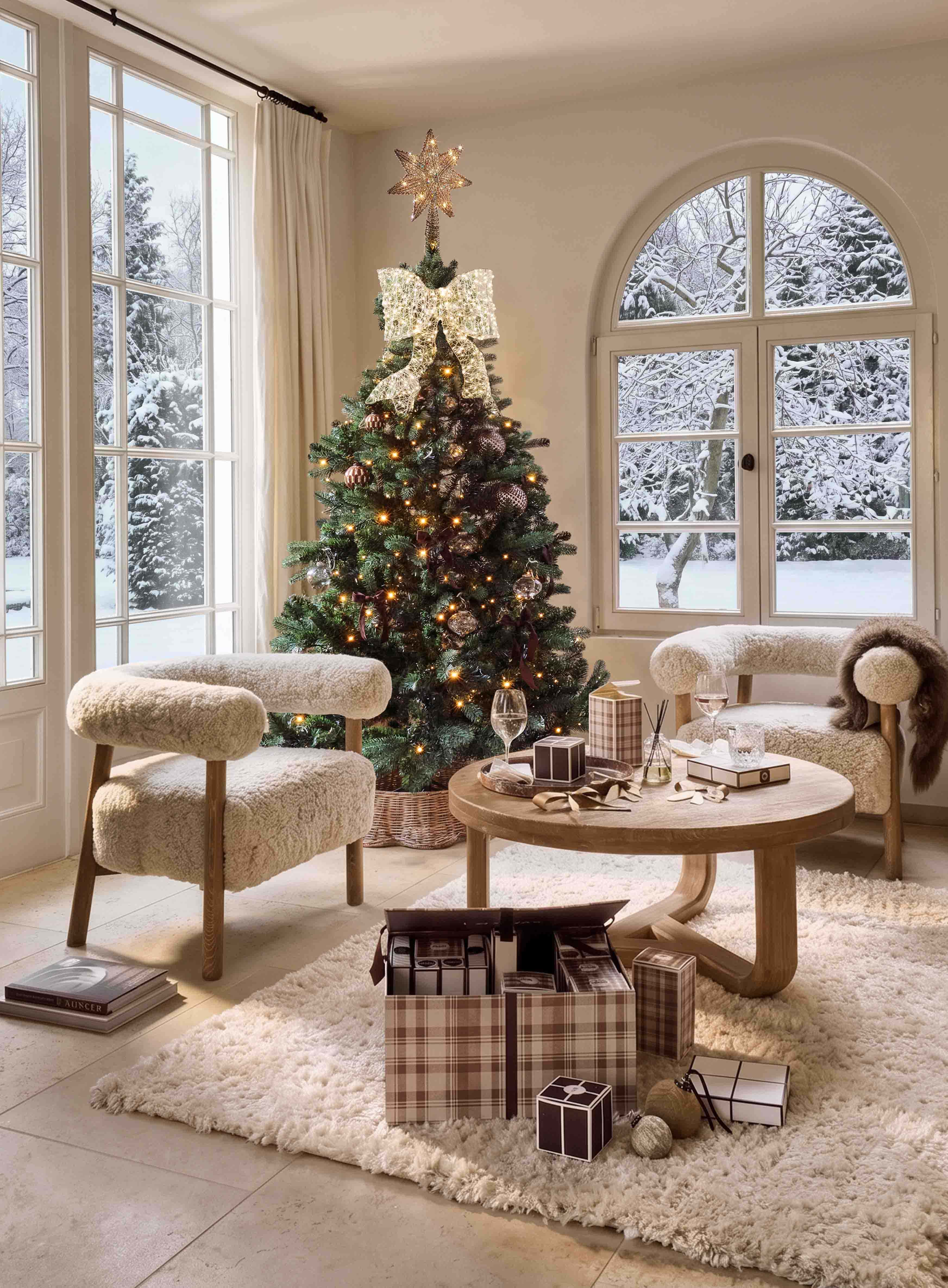 Weihnachtsbaum mit leuchtendem Stern und grosser Schleife in gemütlichem Wohnzimmer mit Blick auf verschneiten Garten