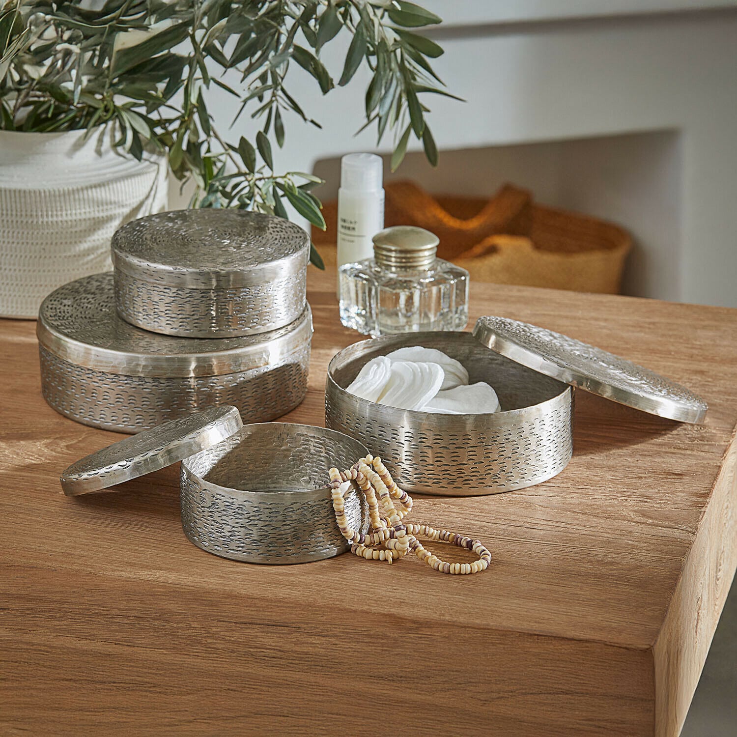 Set mit drei runden Metallbehältern in Silber zum Aufbewahren von Kosmetik und Schmuck auf Holztisch