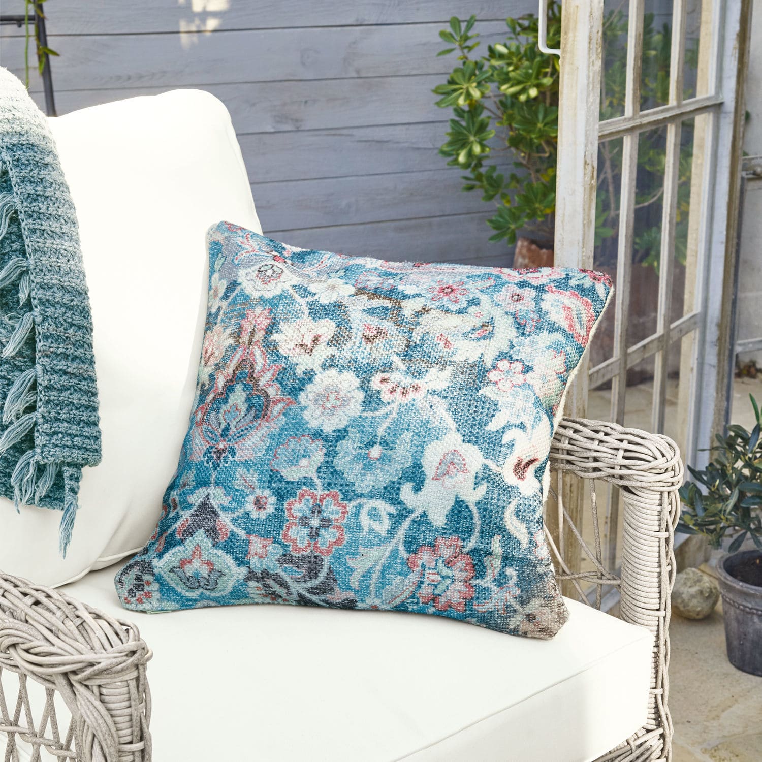 In- & Outdoor-Kissenhülle Obair Dekoratives Kissen aus Stoff mit blau-rosa Blumenmuster auf weissem Rattansessel