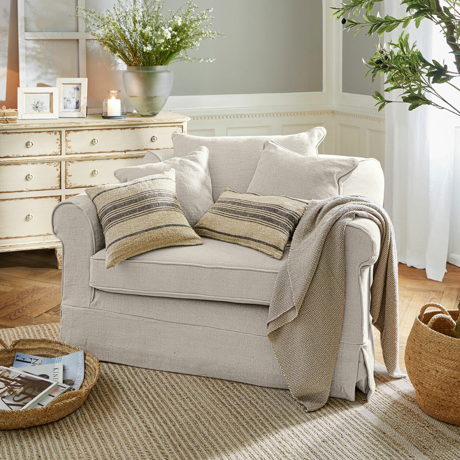Sessel Folsom Beiges Sofa aus Stoff mit gestreiften Kissen und Decke in einem gemütlichen Wohnzimmer mit Naturteppich.