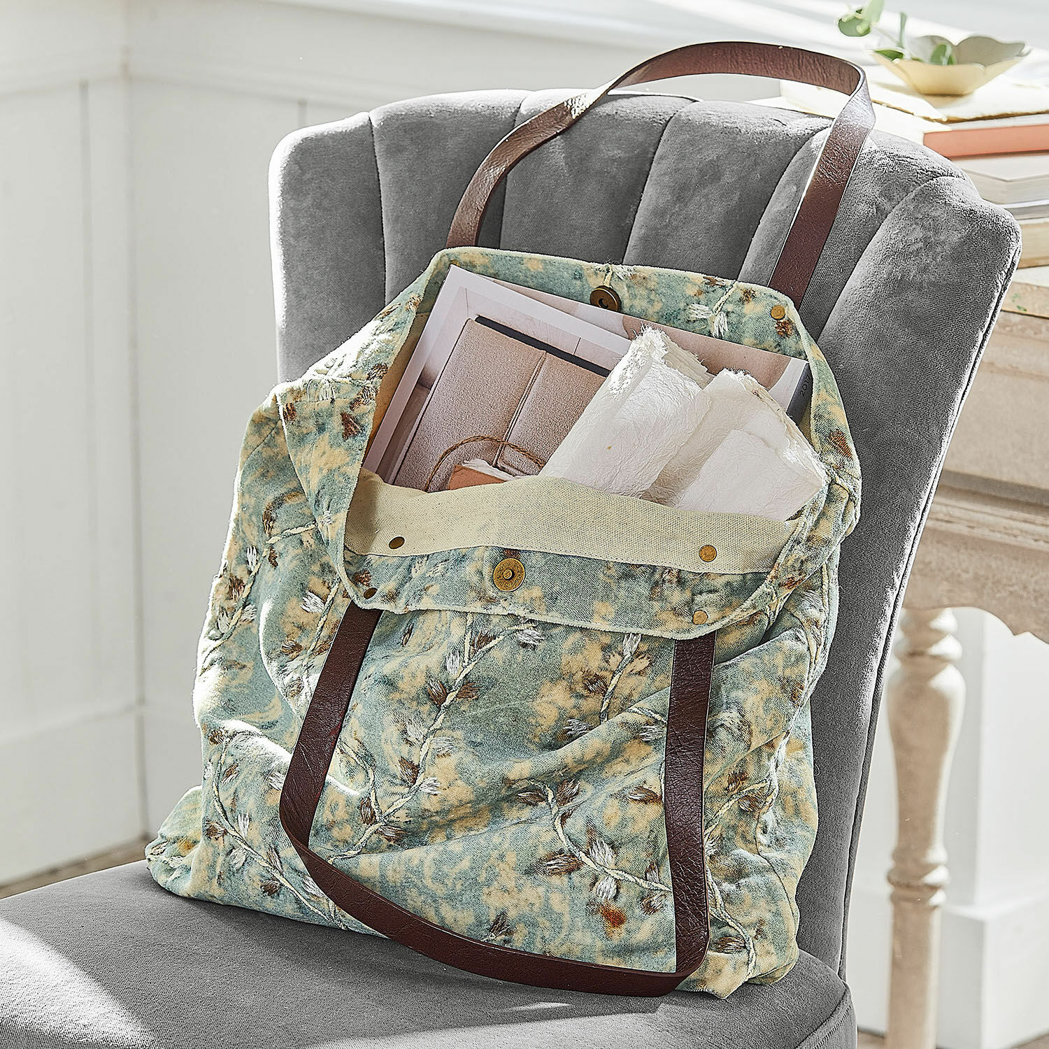 Tasche LaRoux Tasche aus weichem Stoff mit grün-beigem Muster und braunen Griffen auf grauem Stuhl