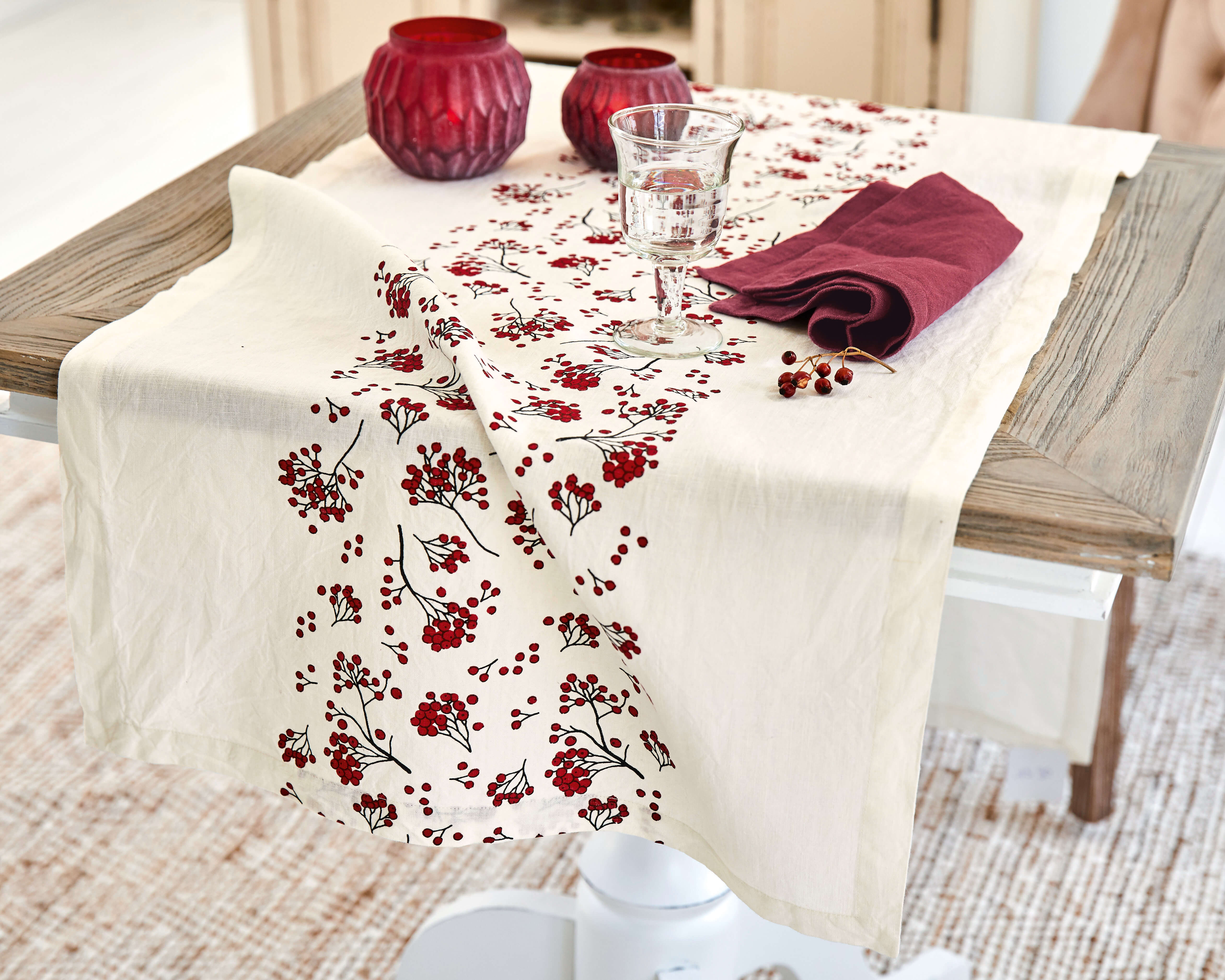 Tischläufer aus Baumwolle in Creme mit rotem Beerenmuster und dekorativen roten Kerzenhaltern