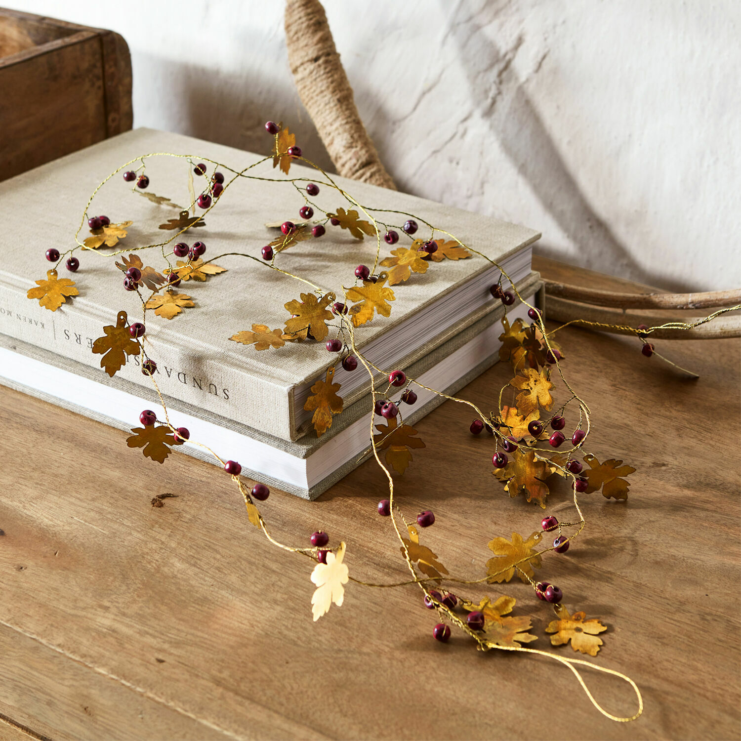 Girlande Liezel Dekorative Girlande mit goldfarbenen Metallblättern und roten Beeren auf Holztisch
