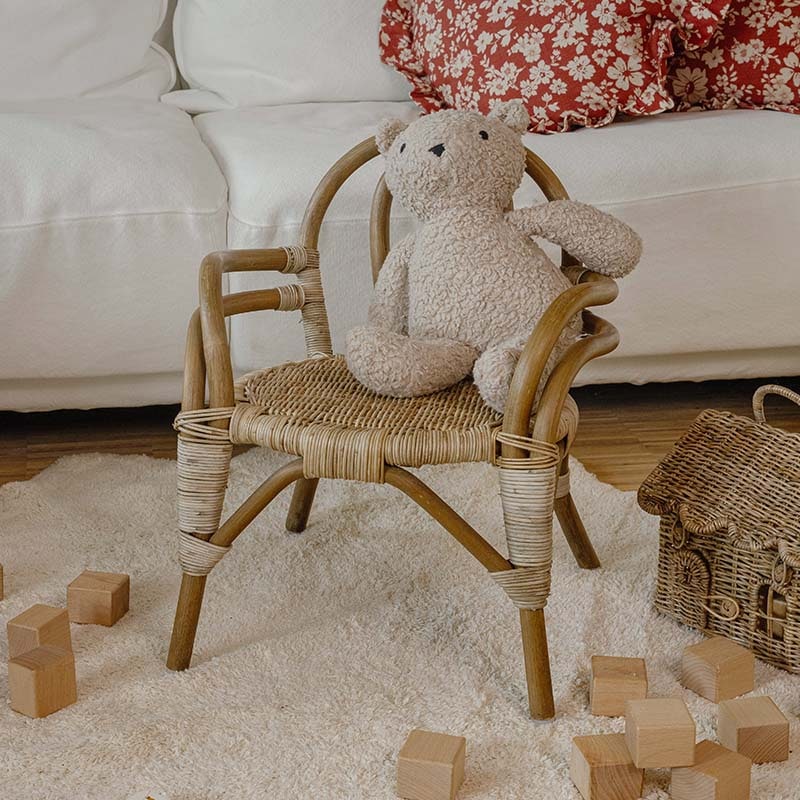 Kinderstuhl aus Rattan mit beigem Plüschbär auf hellem Teppich und Holzbausteinen