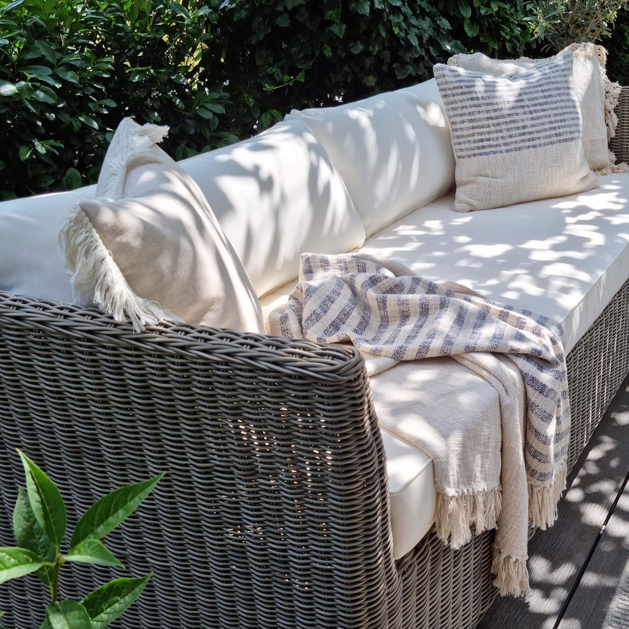 Gartensofa aus grauem Rattan mit cremefarbenen Kissen und beigem gestreiften Plaid