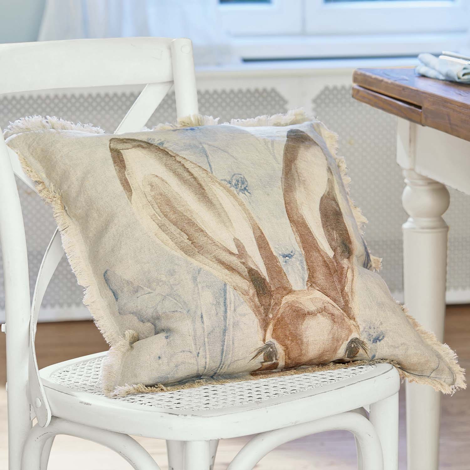 Beiges Leinenkissen mit Hasenohren-Motiv und Fransen auf weissem Stuhl im Wohnzimmer