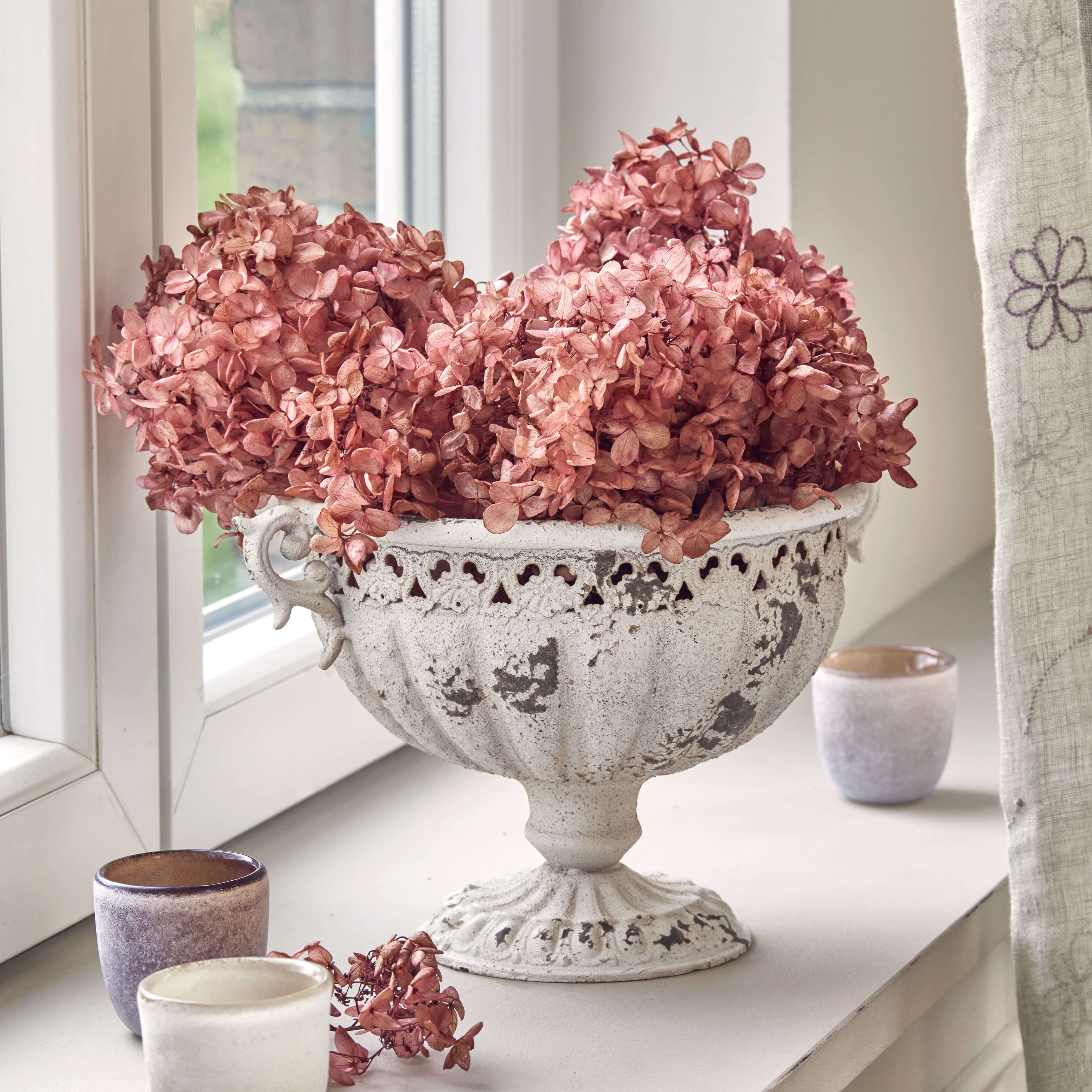 Weiße Metallschale mit antikem Look und getrockneten rosa Blumen auf Fensterbank