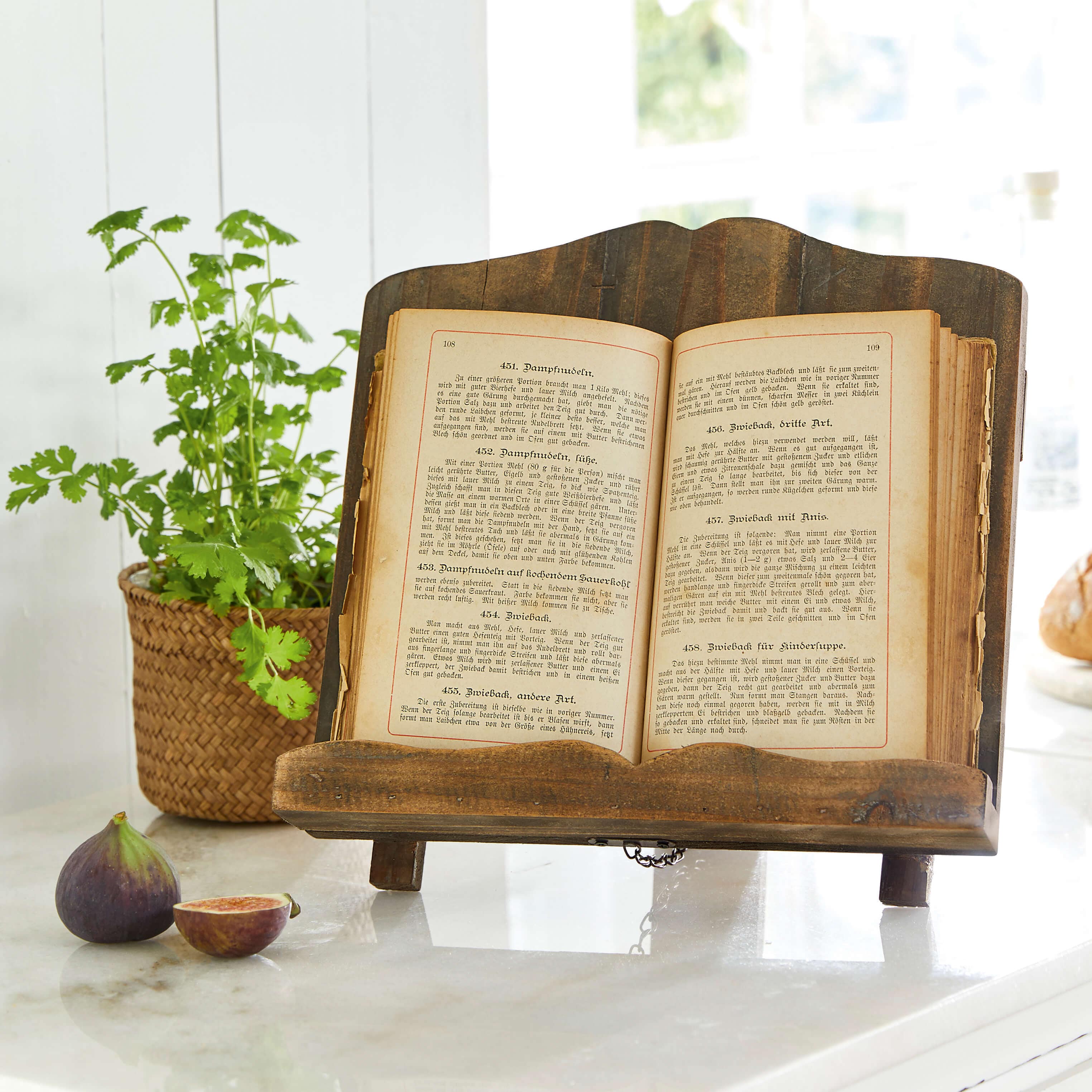 Dunkler Holzbuchhalter mit offenem altem Kochbuch auf Marmorarbeitsfläche