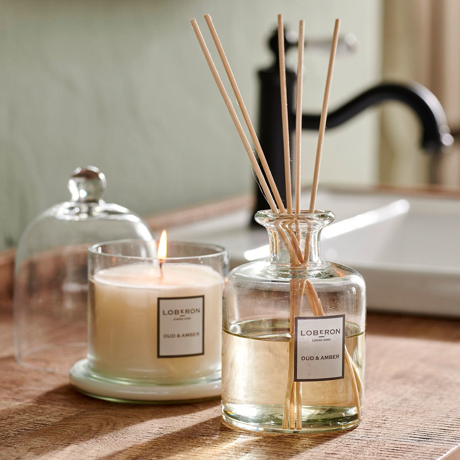 Duftset Vanis Glas-Duftkerze und Diffusor Oud & Amber auf Holzplatte im Badezimmer