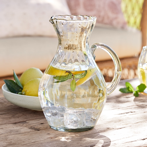 Glaskrug mit Wasser, Eiswürfeln und Zitronenscheiben auf Holztisch, erfrischendes Sommergetränk