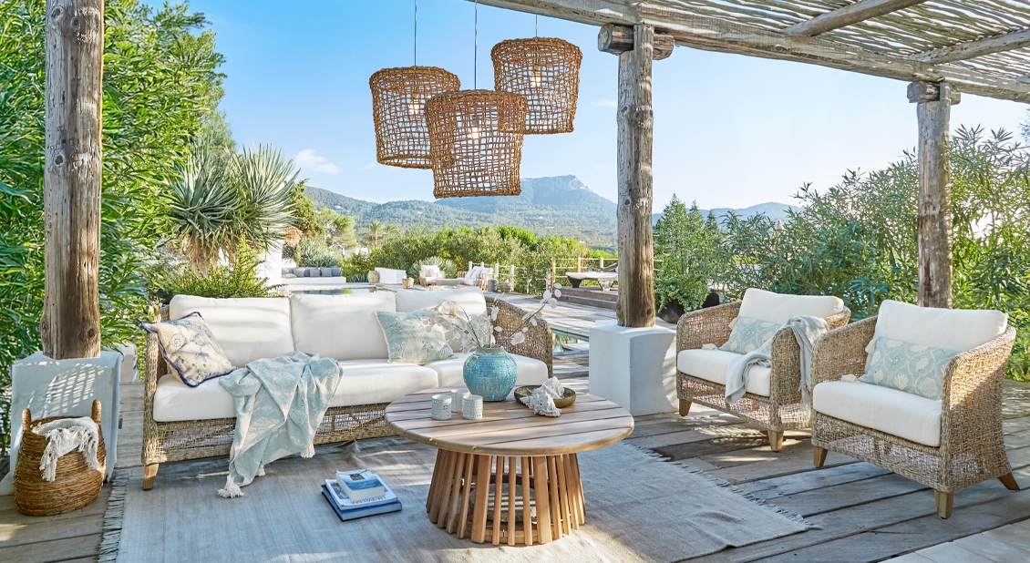Outdoor-Rattansitzgruppe in Natur mit weissen Polstern und rundem Holztisch auf Terrasse mit Bergsicht