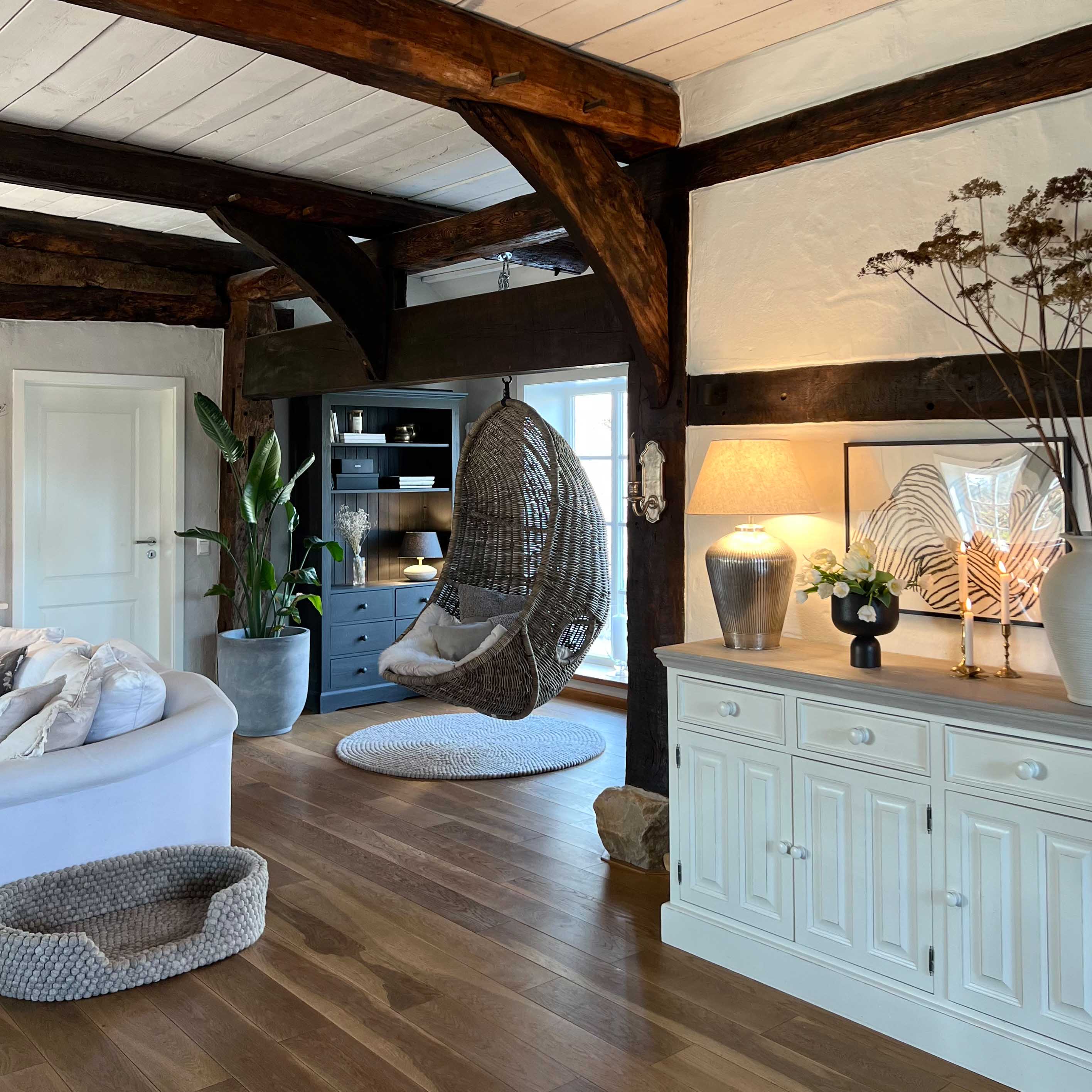 Hängesessel aus grauem Rattan im gemütlichen Wohnzimmer mit Holzboden und weissem Sideboard