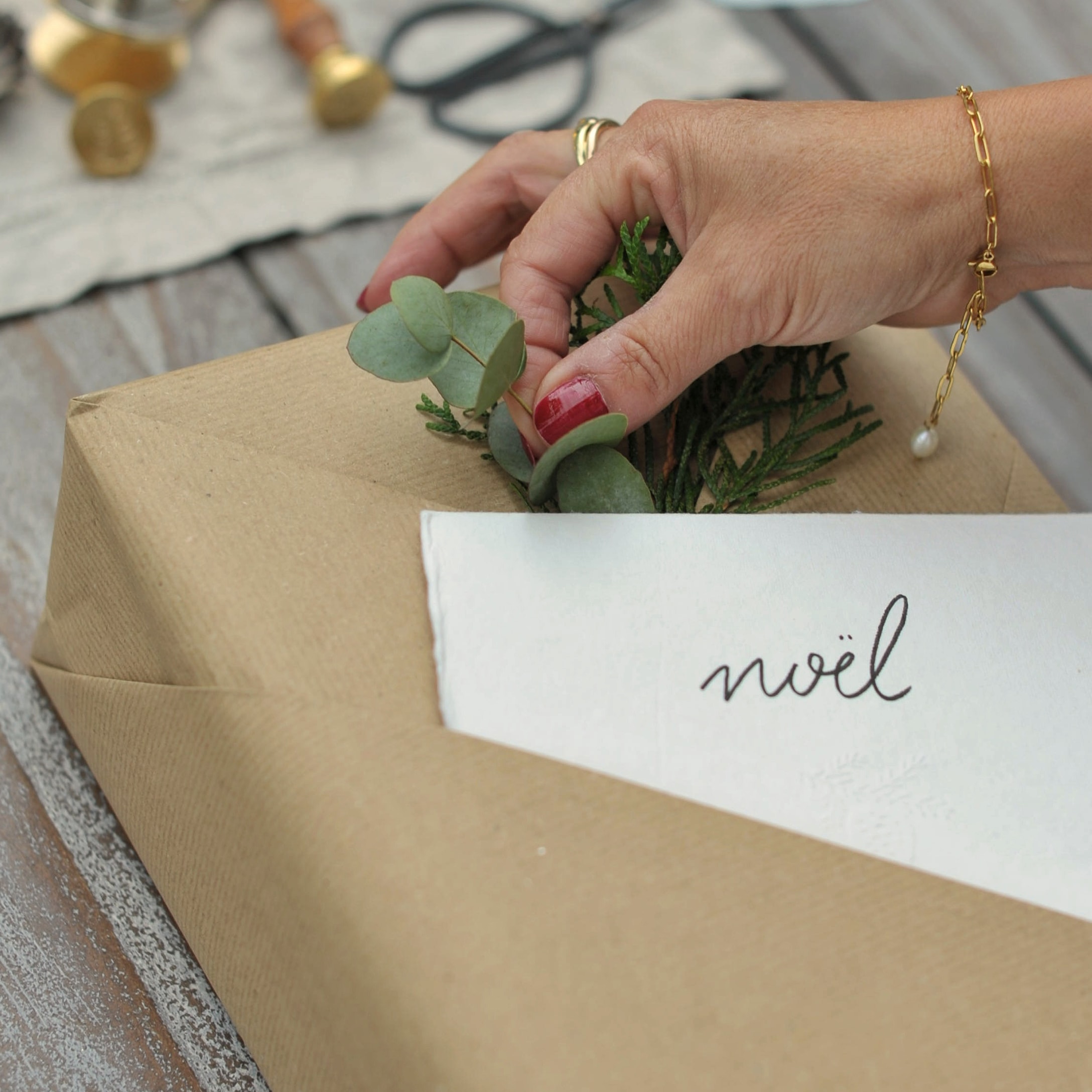 Handdekoriertes Geschenk in braunem Papier mit grünen Blättern und Karte mit Schriftzug Noël