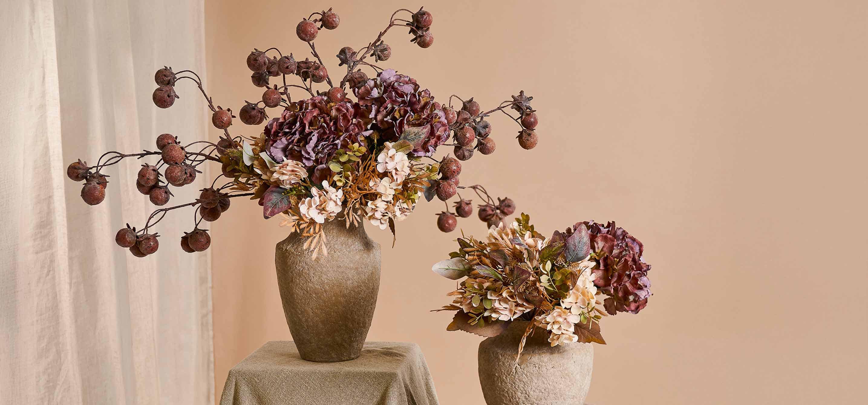 Zwei dekorative beige Steinvase mit herbstlichen Blumen und getrockneten Früchten in warmen Farben für Wohnraum