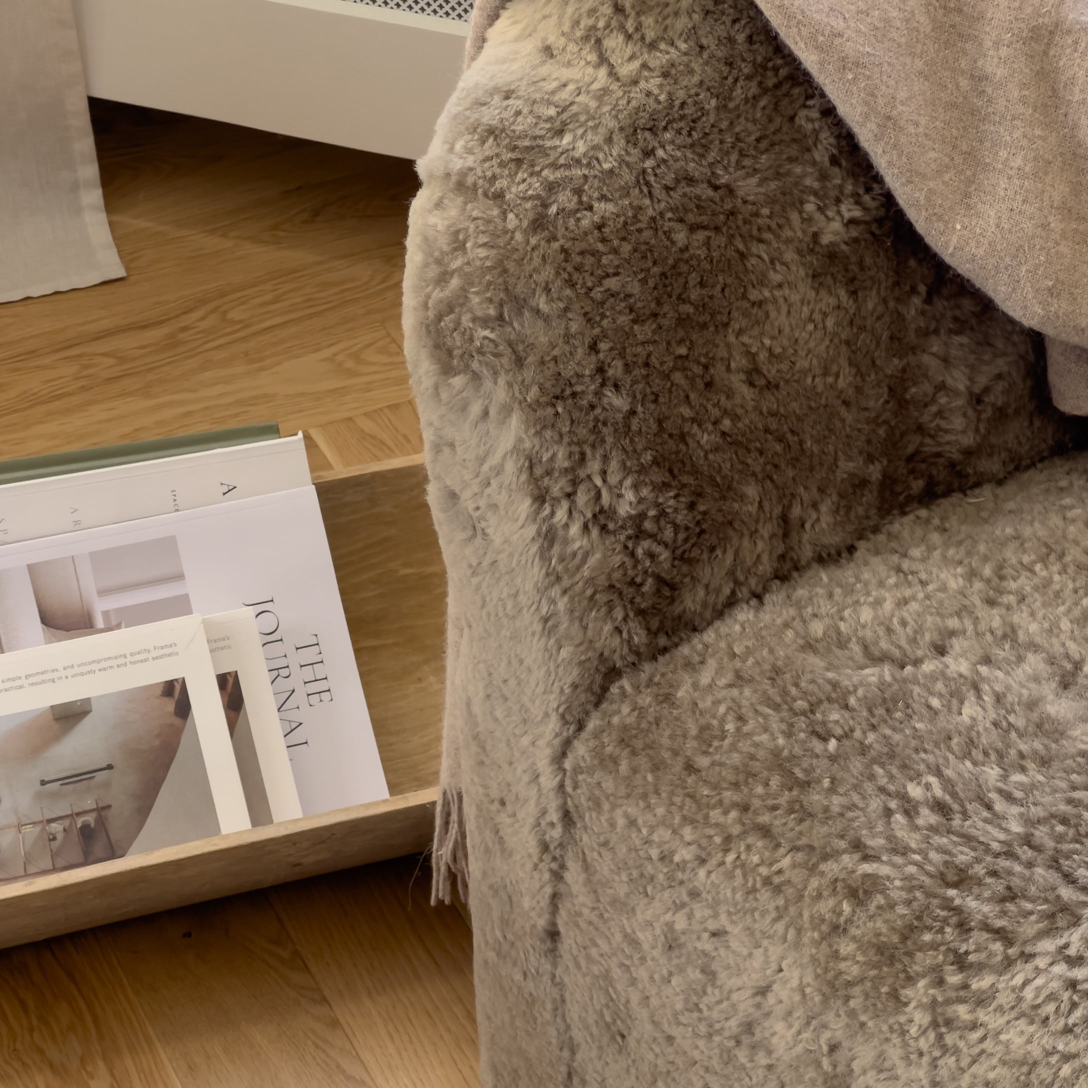 Weiche beige Fell-Kuscheldecke auf Sessel neben Holztablett mit Zeitschriften, gemütliches Wohnaccessoire