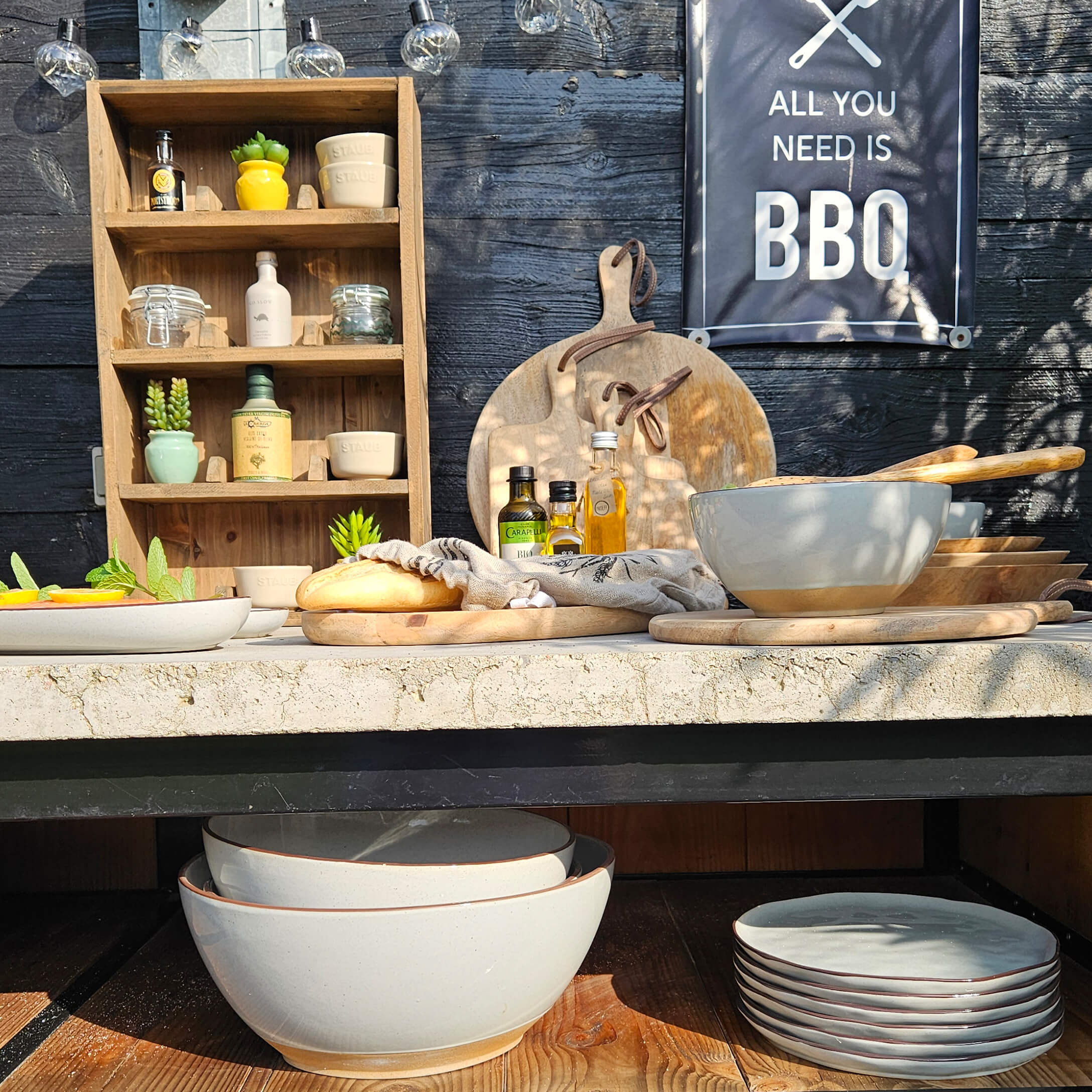 Beige Keramikgeschirr mit Holzschneidebrettern und Ölflaschen auf einem Grilltisch im Freien