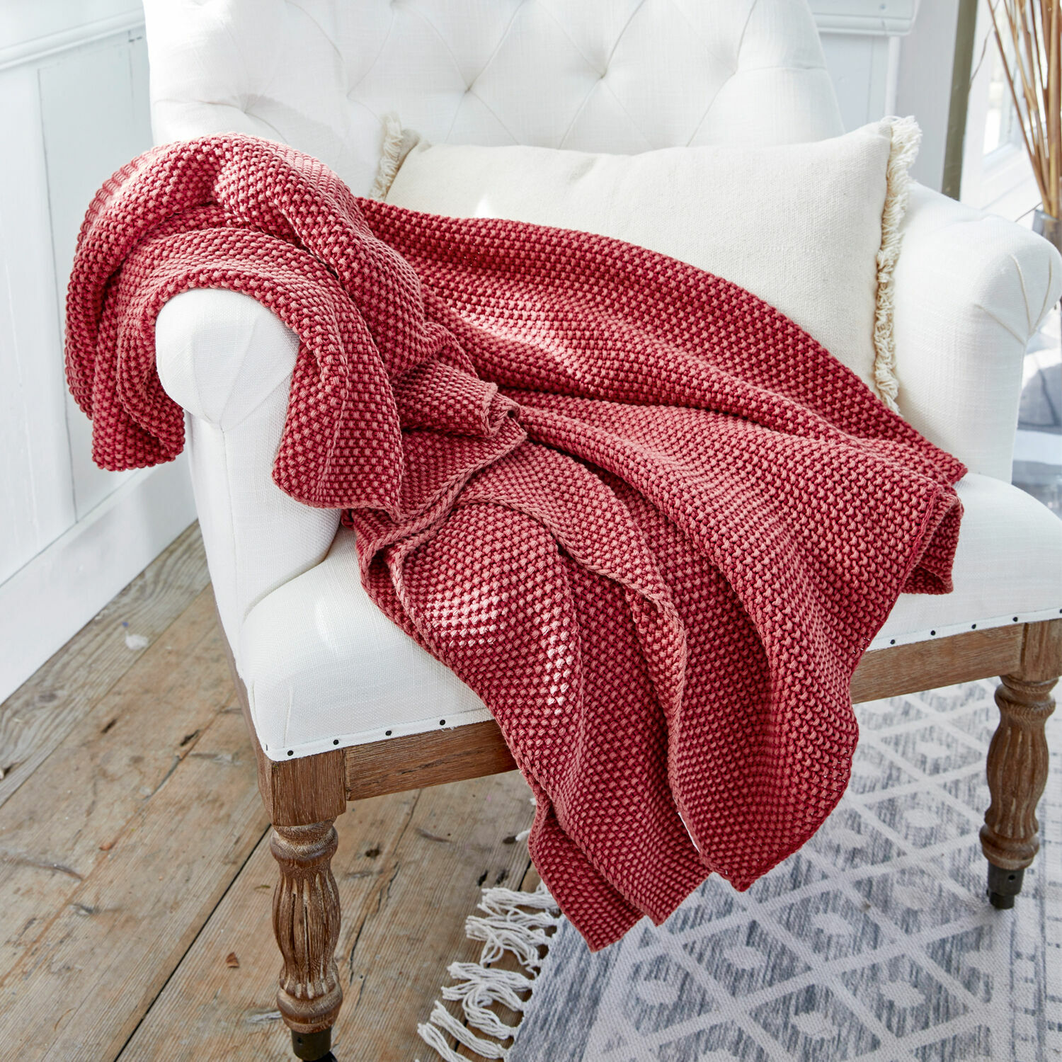 Plaid Amberley Rote gestrickte Kuscheldecke aus weichem Material auf weissem Sessel in hellem Raum