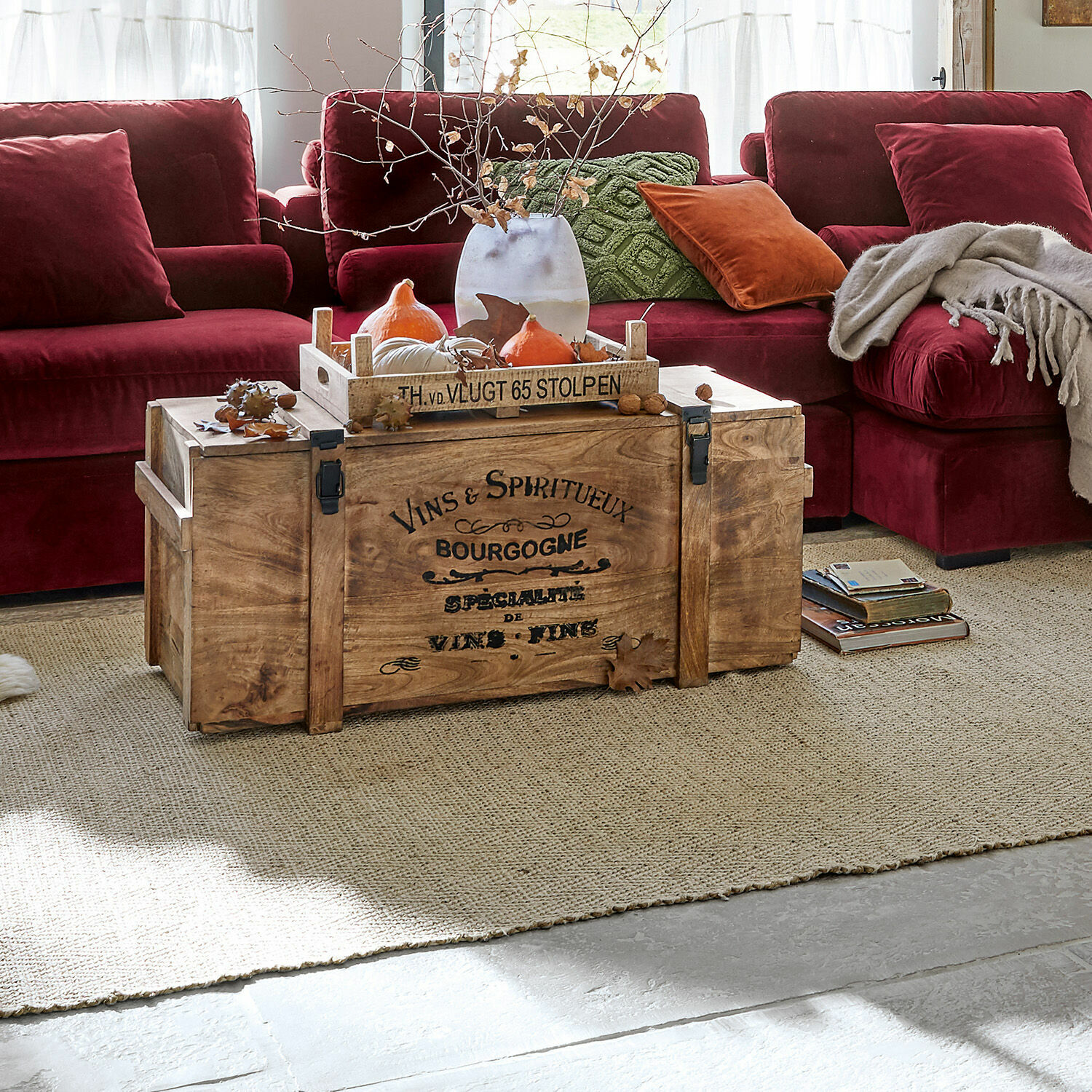 Truhe Eskeny Holztruhe mit Aufdruck auf Teppich vor rotem Sofa mit Kissen und Decke im Wohnzimmer