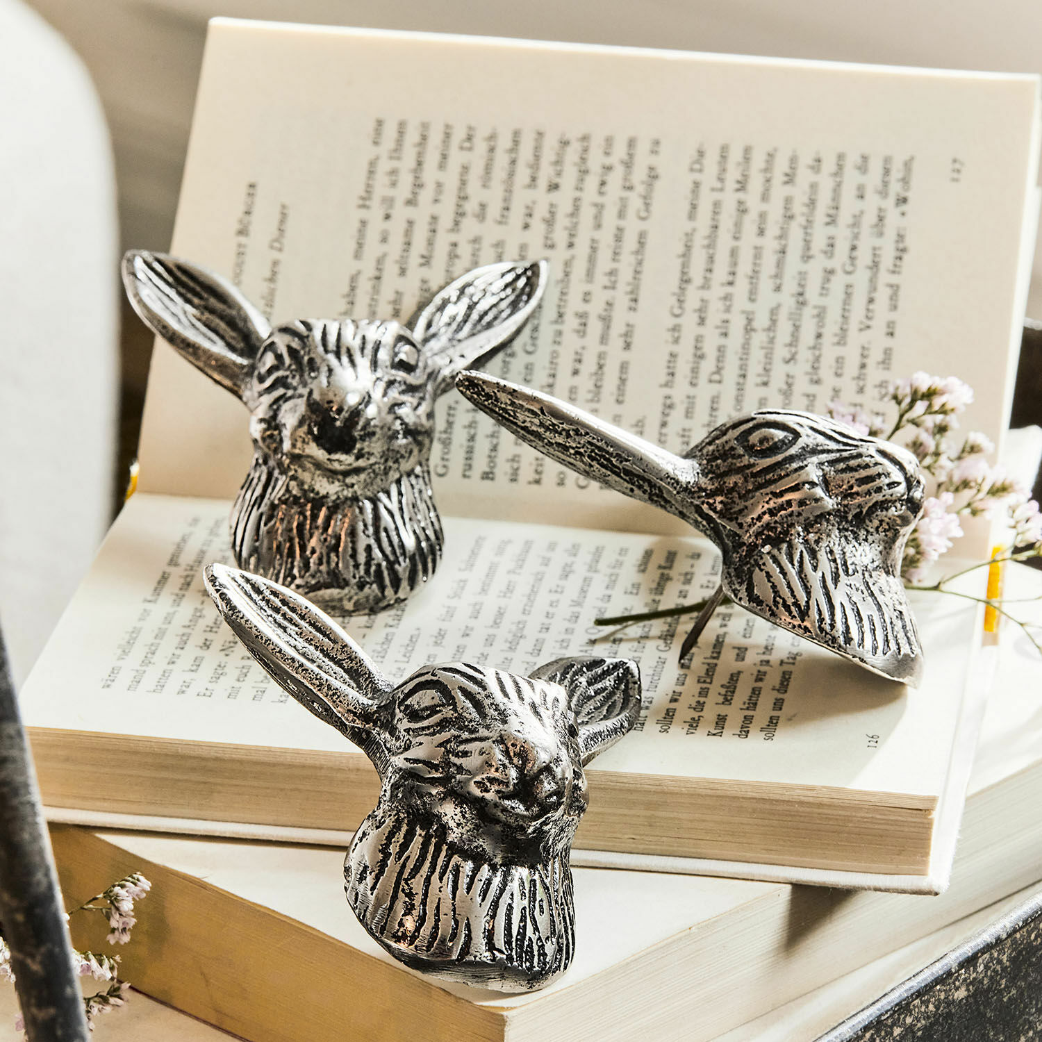 Deko-Pin 3er Set Gimont Drei silberne Metalldekorationen in Hasenkopf-Form auf offenem Buch, stilvolle Wohnaccessoires