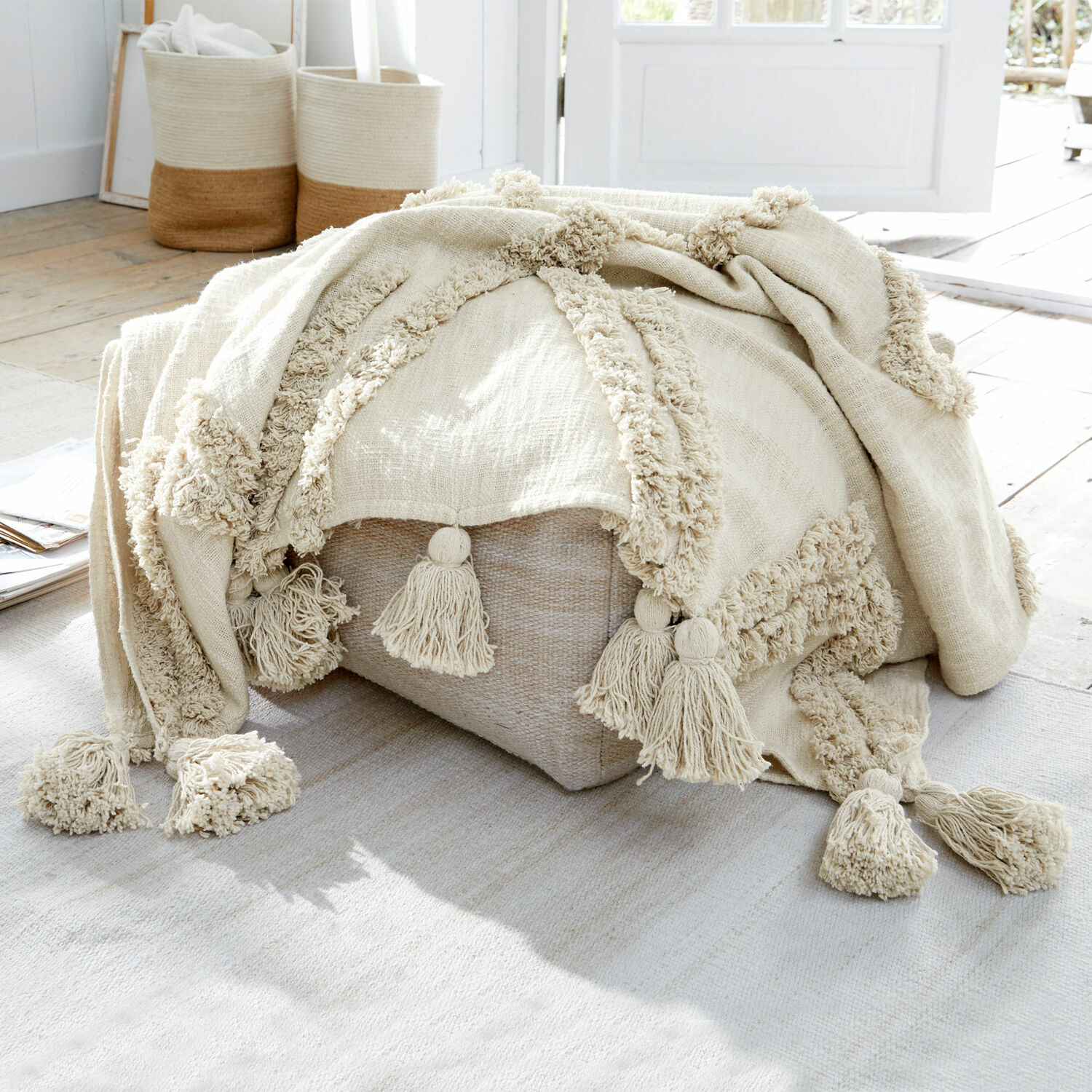 Plaid Linares Beige Baumwolldecke mit Quasten auf hellem Pouf in natürlichem, hellem Raum
