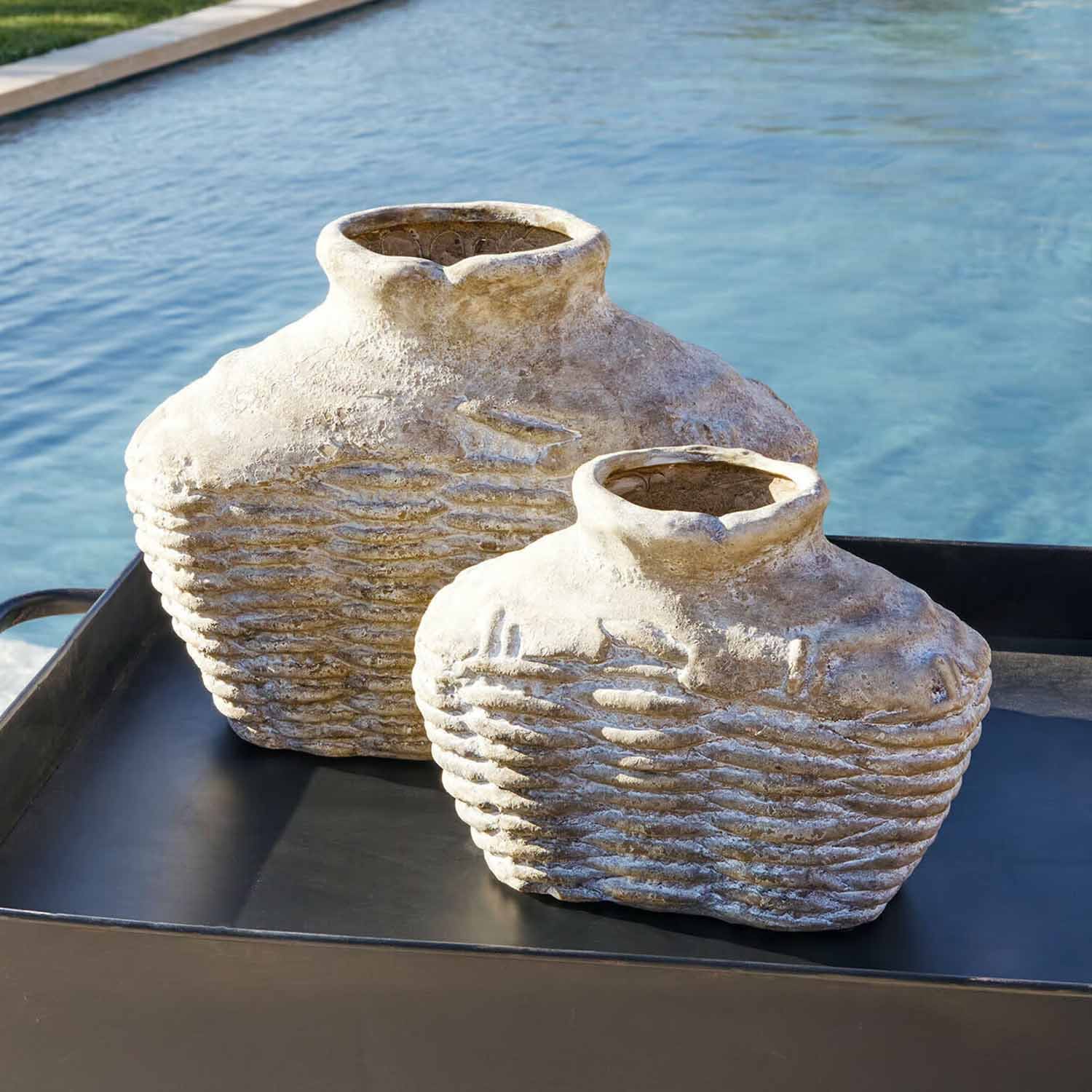 Zwei rustikale Vasen aus beigem Stein auf schwarzem Tablett neben einem Pool