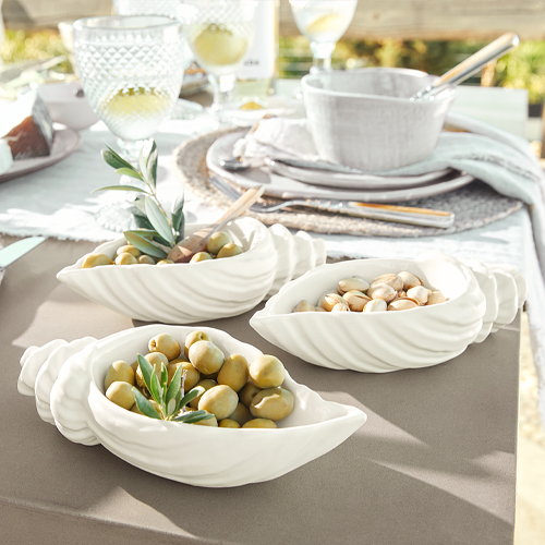 Weisse Keramikschalen in Muschelform mit Oliven und Nüssen auf Gartentisch