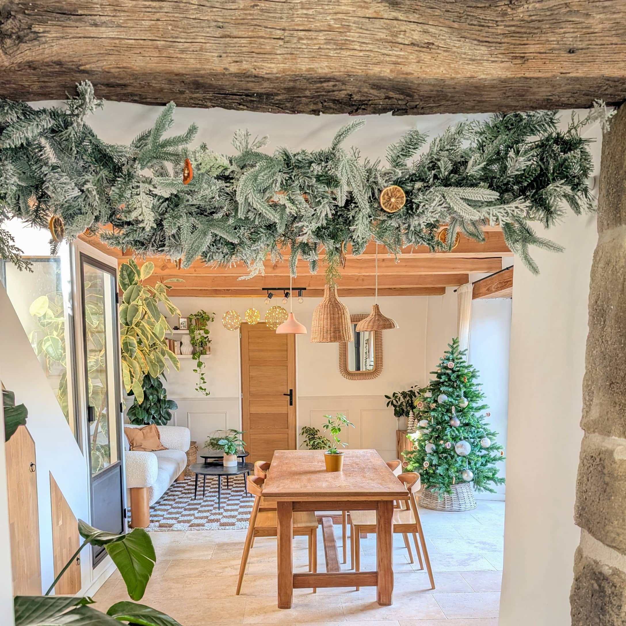 Weihnachtsdekoration mit grünen Zweigen und getrockneten Orangenscheiben in einem hellen Wohnzimmer mit Holztisch