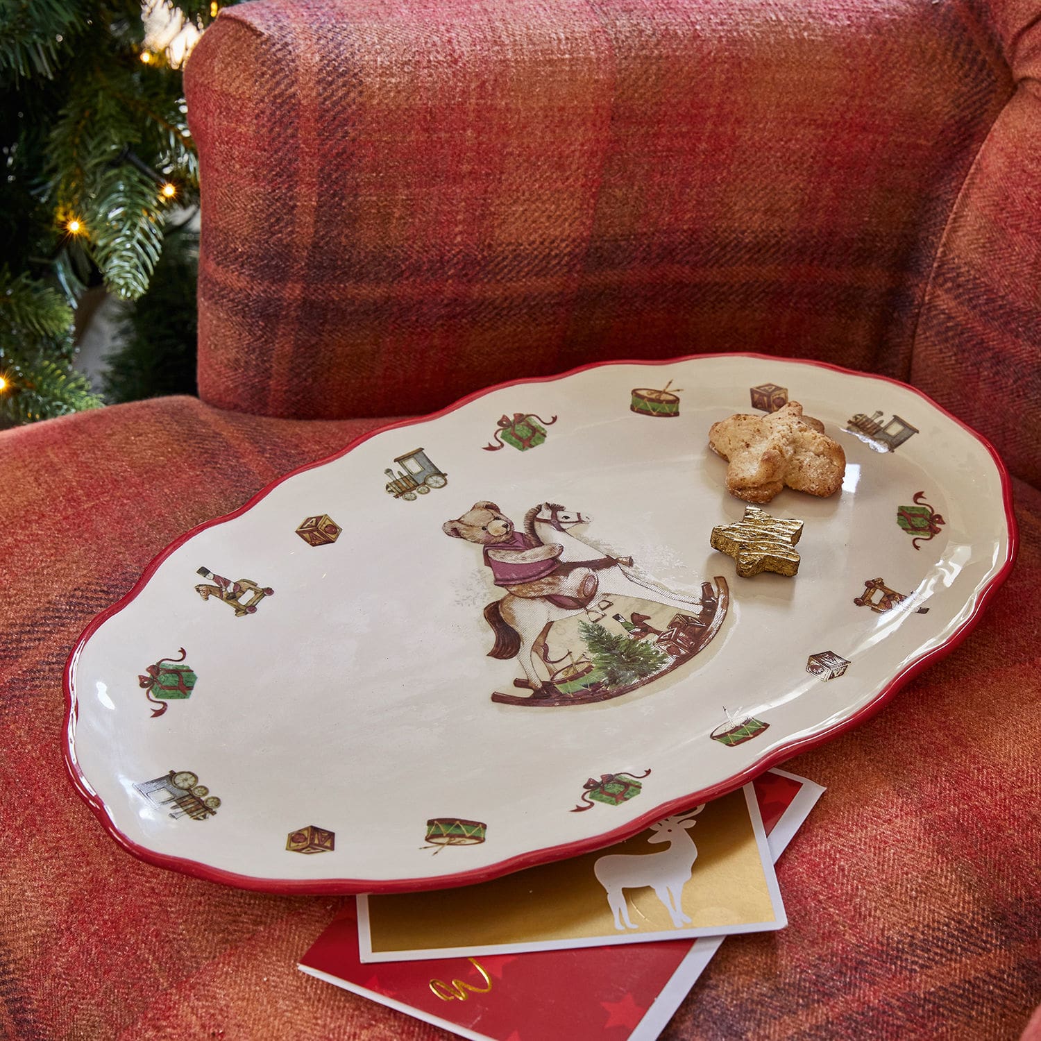 Platte Troms Keramikteller mit Weihnachtsmotiv: Bär auf Schaukelpferd und rotem Rand auf rotem Sofa