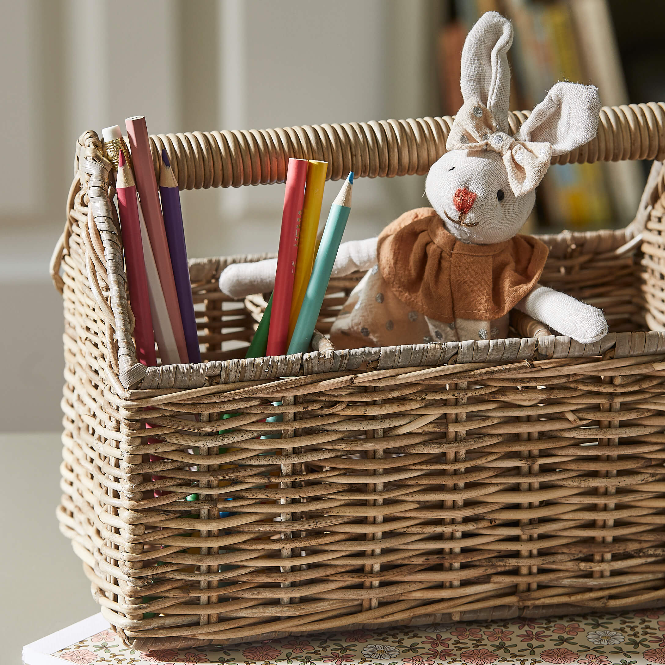 Wiklinerkorb mit bunten Buntstiften und beigem Stoffhasen mit Kleidchen