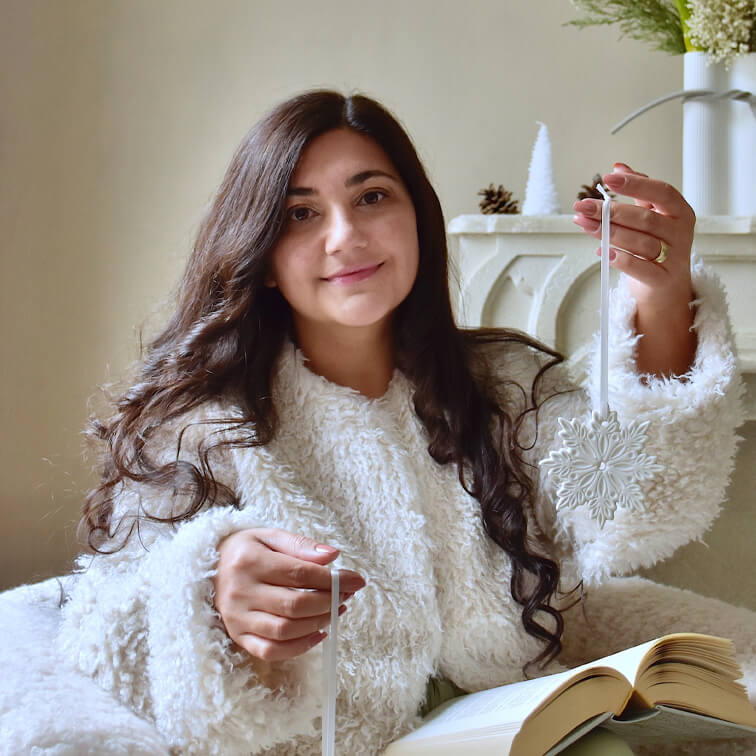Frau in weissem flauschigem Pullover hält weissen Schneeflocken-Weihnachtsschmuck mit offenem Buch auf dem Schoss